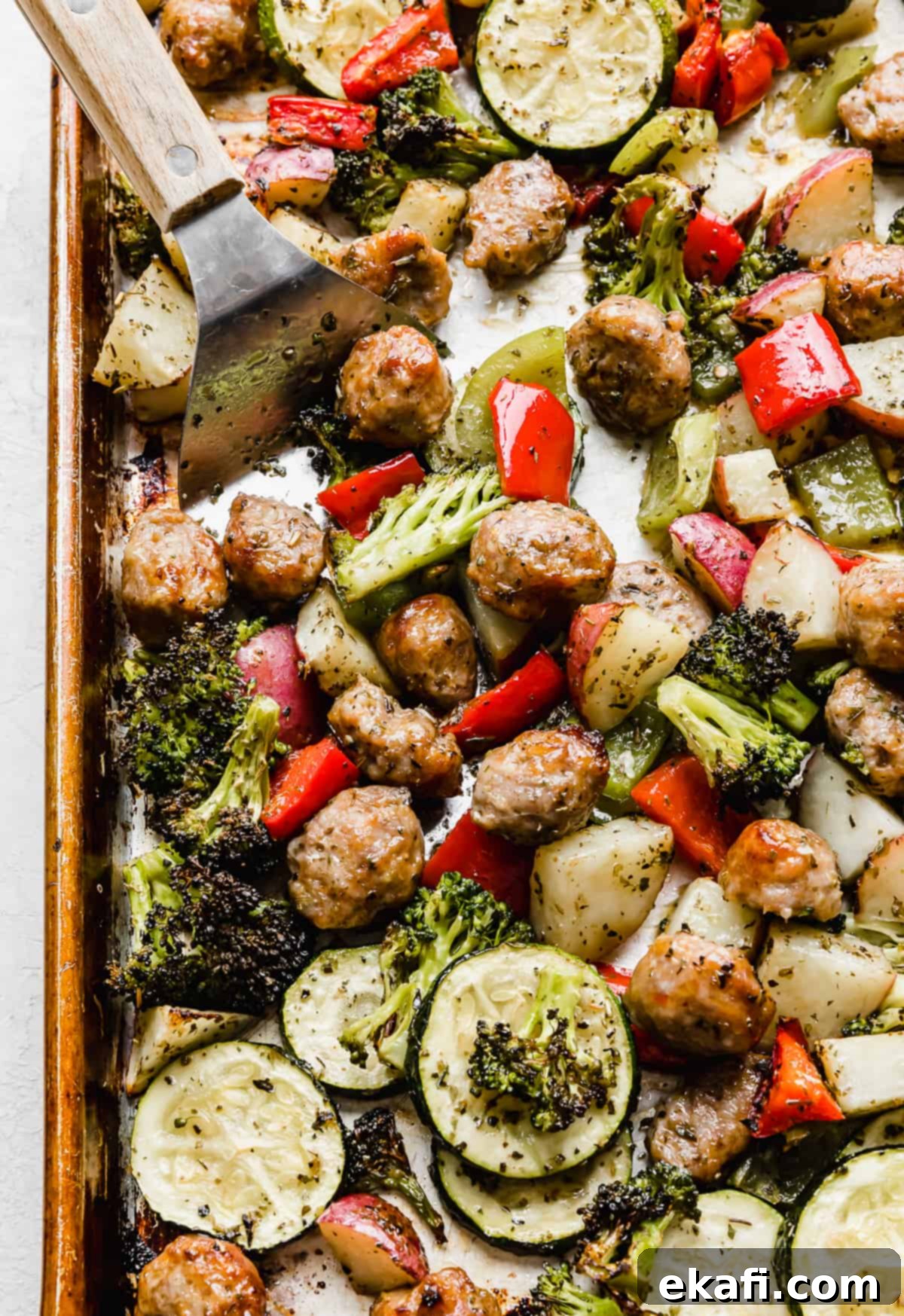 One Pan Roasted Italian Sausage and Vibrant Vegetables 2 Sheet Pan Sausage and Veggies with a metal spatula scooping up some of the veggies.
