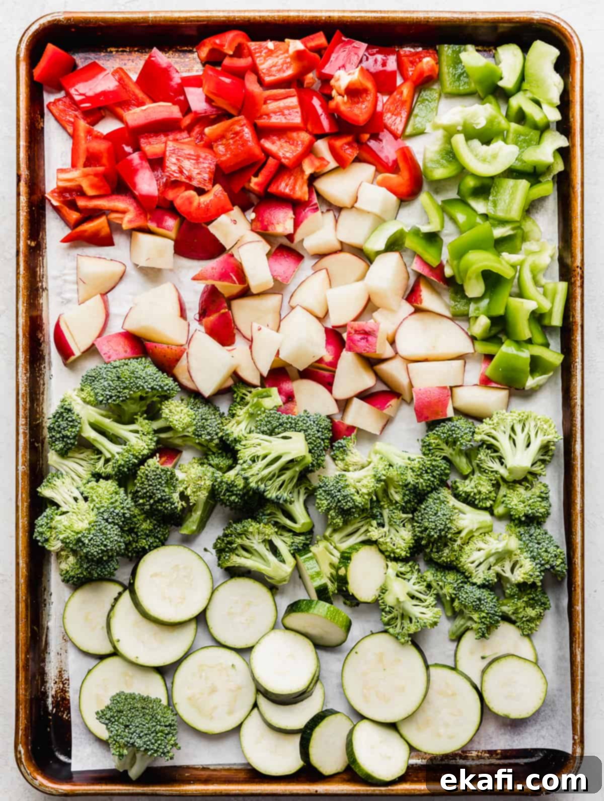One Pan Roasted Italian Sausage and Vibrant Vegetables 4 A baking sheet with red and green peppers, cut potatoes, broccoli florets and coin zucchini slices.