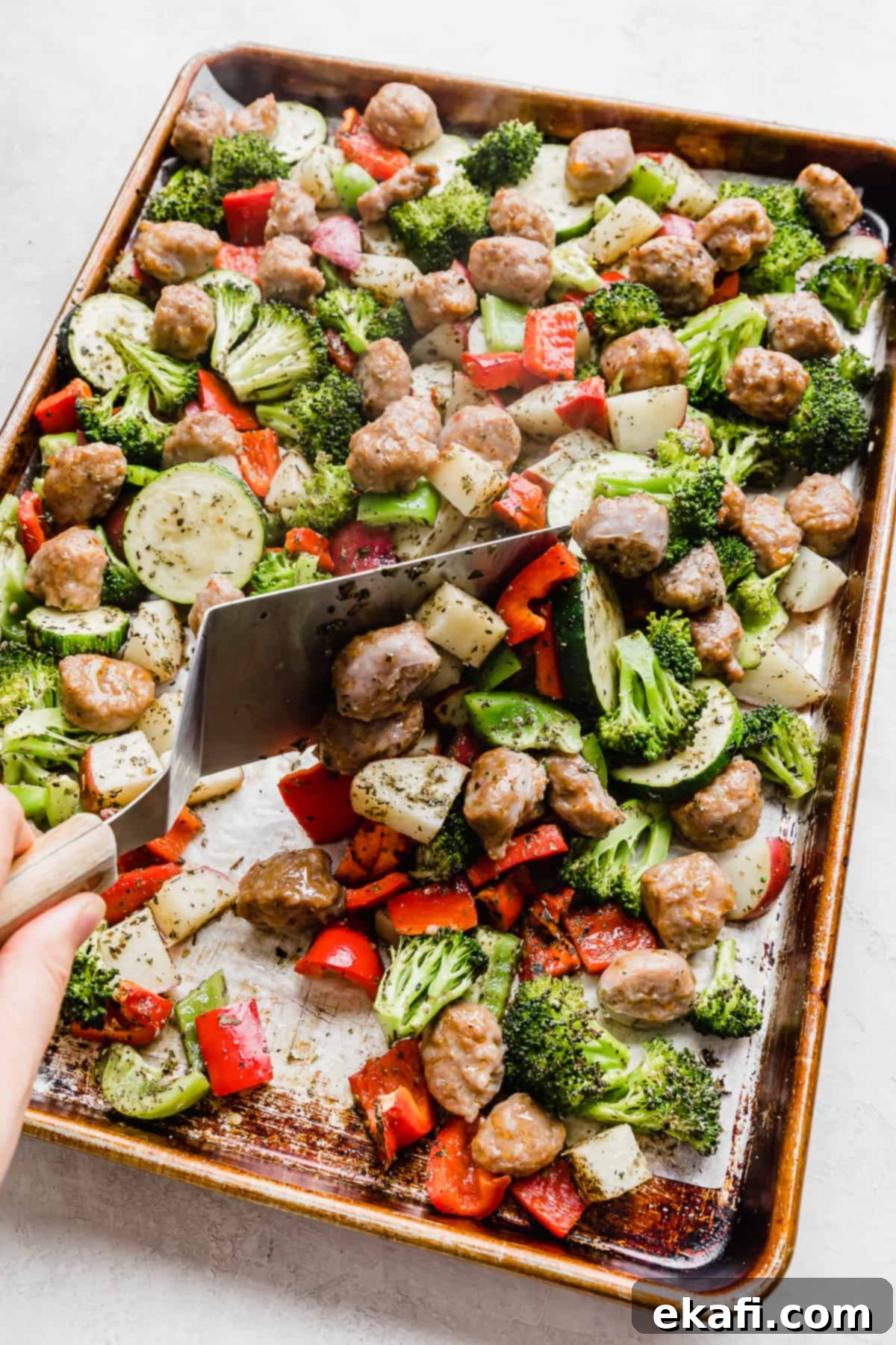 One Pan Roasted Italian Sausage and Vibrant Vegetables 8 A metal spatula turning over sausage and veggies on a sheet pan.