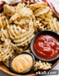 Πατάτες Waffle στη Φριτέζα Αέρος 9 Πατάτες βάφλα σε καφέ πιάτο με μπολ κέτσαπ και σάλτσα chick fil a δίπλα τους.