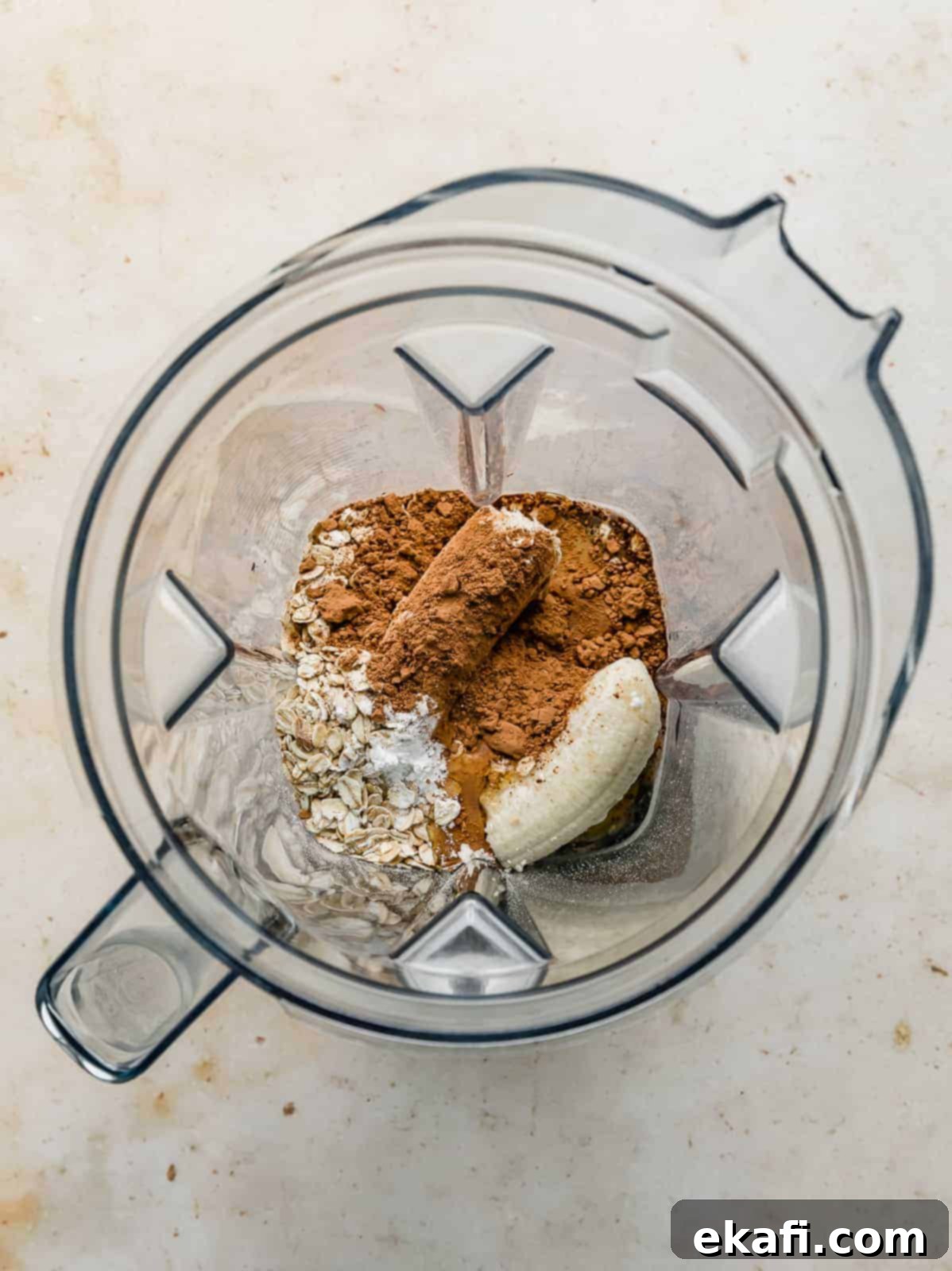 Chocolate Baked Oats Perfection 4 An overhead photo of a blender with a banana, oats, and cocoa unblended.