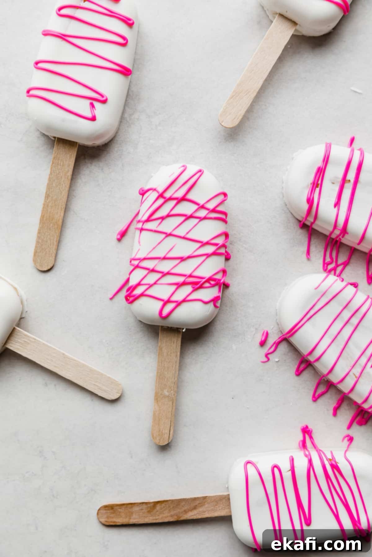 Κεκάκια Παγωτό 12 Λευκά Cakesicles καλυμμένα με σοκολάτα με ροζ σοκολατένιο σιρόπι, σε λευκό φόντο.