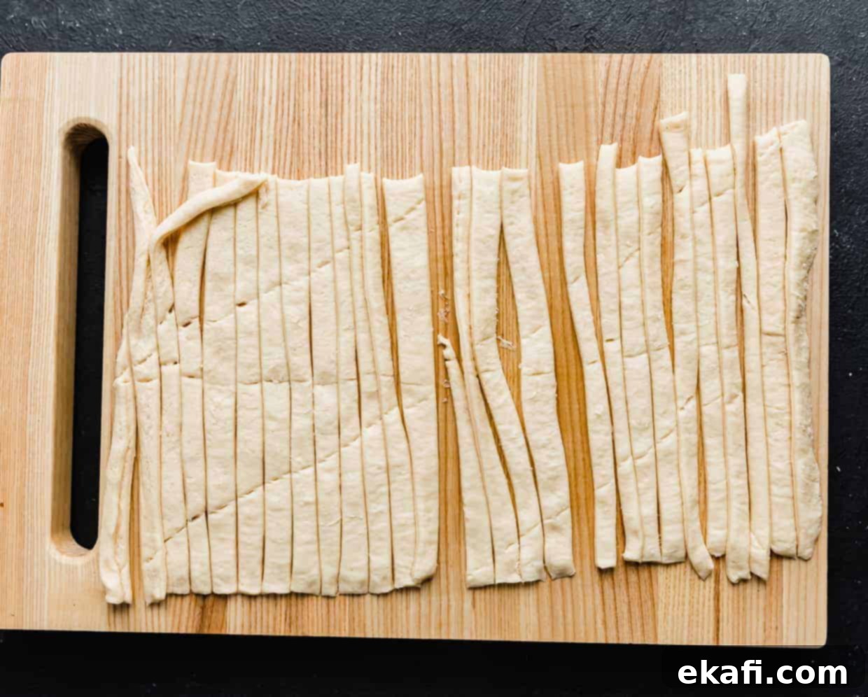 Mummy Hot Dogs 5 A wooden cutting board with a crescent roll sheet cut into strips on it.