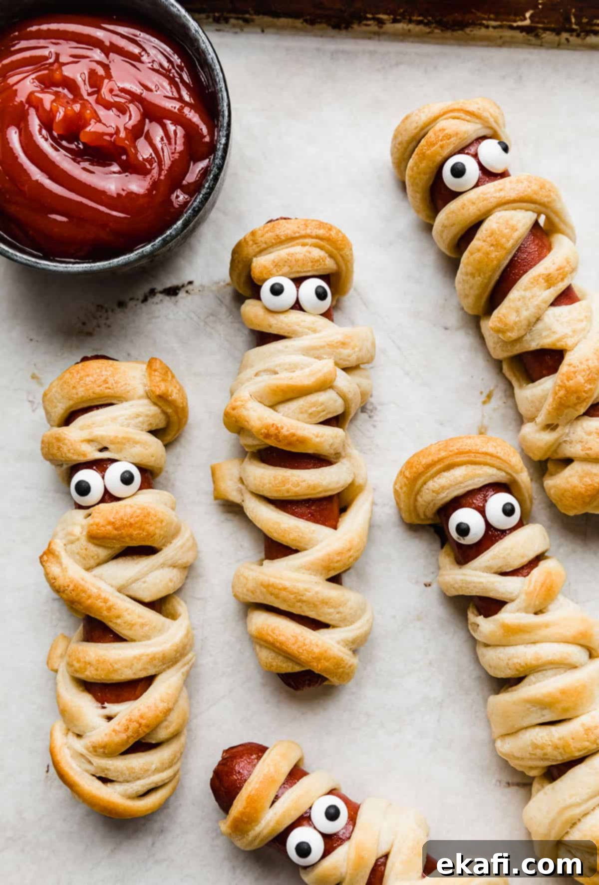 Mummy Hot Dogs 9 Mummy Hot Dogs on a parchment lined baking sheet with candy eyes on the hot dog.