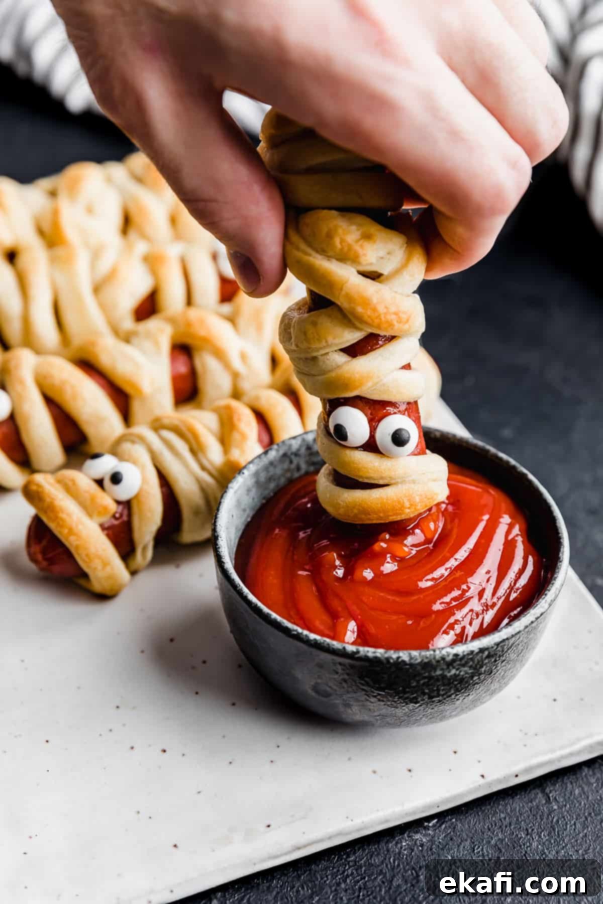 Mummy Hot Dogs 10 A hand dipping a Mummy Hot Dog into a bowl of ketchup.