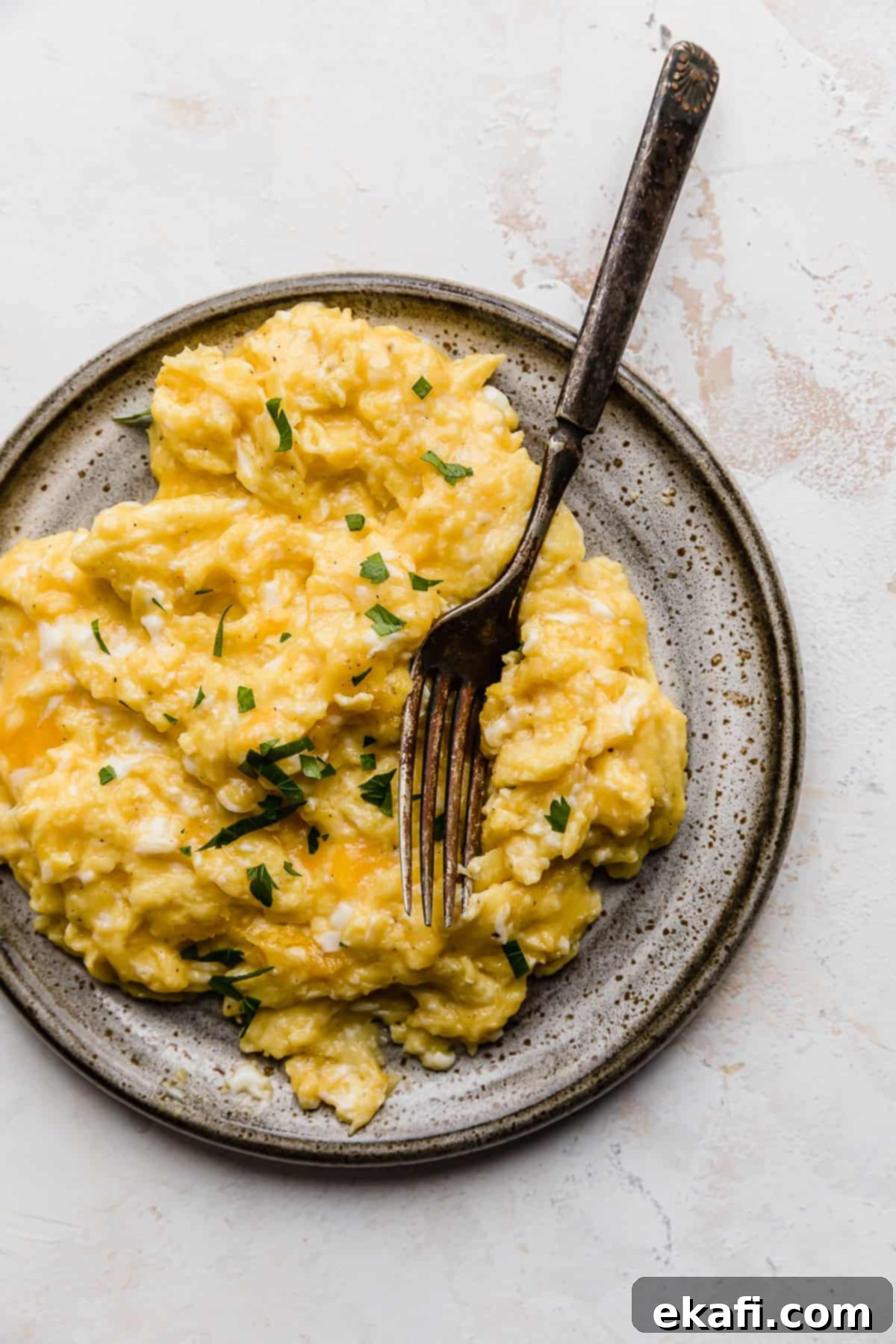 Golden Cheese Scramble 2 A serving of fluffy, golden cheesy scrambled eggs on a gray plate, garnished with fresh herbs, with a fork beside it.