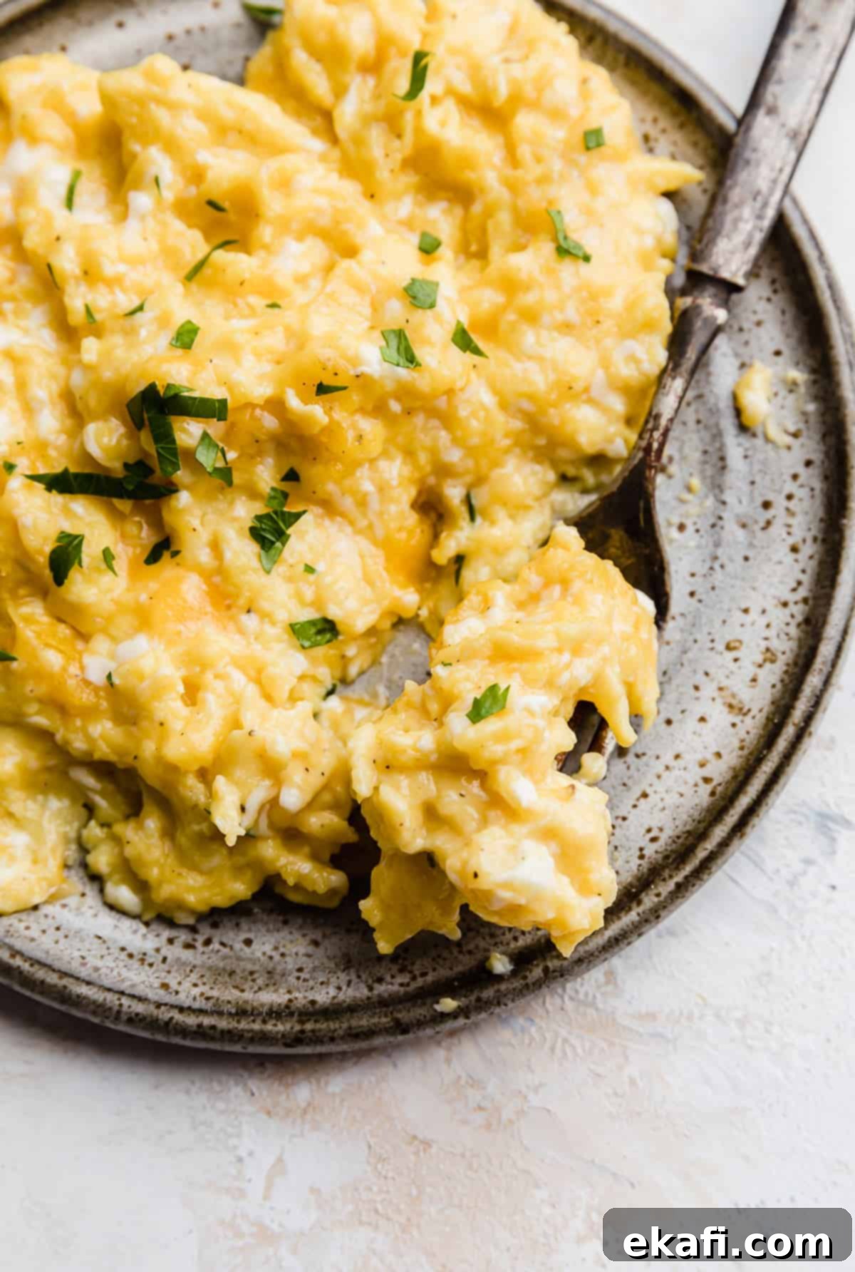 Golden Cheese Scramble 9 A close-up of a generous serving of perfectly fluffy and cheesy scrambled eggs, beautifully garnished with fresh green parsley, on a light gray plate.