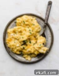 Golden Cheese Scramble 10 A gray plate full of golden, fluffy Cheesy Scrambled Eggs that have been garnished with fresh green parsley.