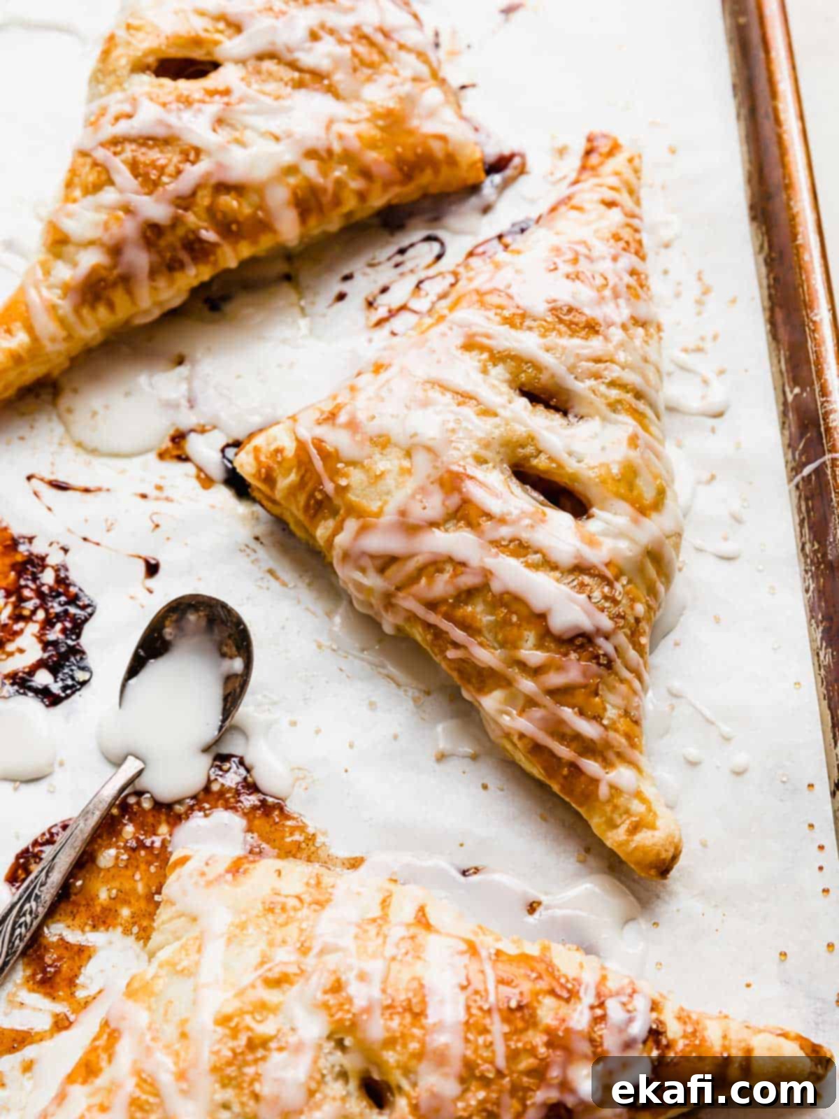 Flaky Apple Turnovers 2 Puff Pastry Apple Turnovers on a white parchment lined baking sheet, drizzled with glaze.