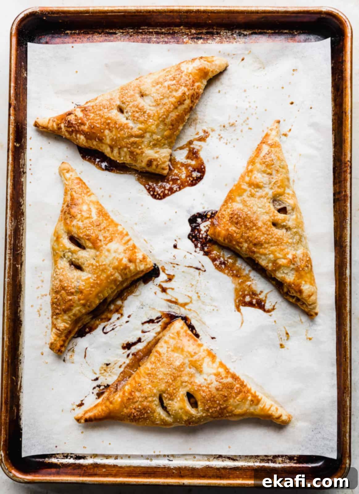 Flaky Apple Turnovers 12 Golden brown Puff Pastry Apple Turnovers on a parchment lined baking sheet.