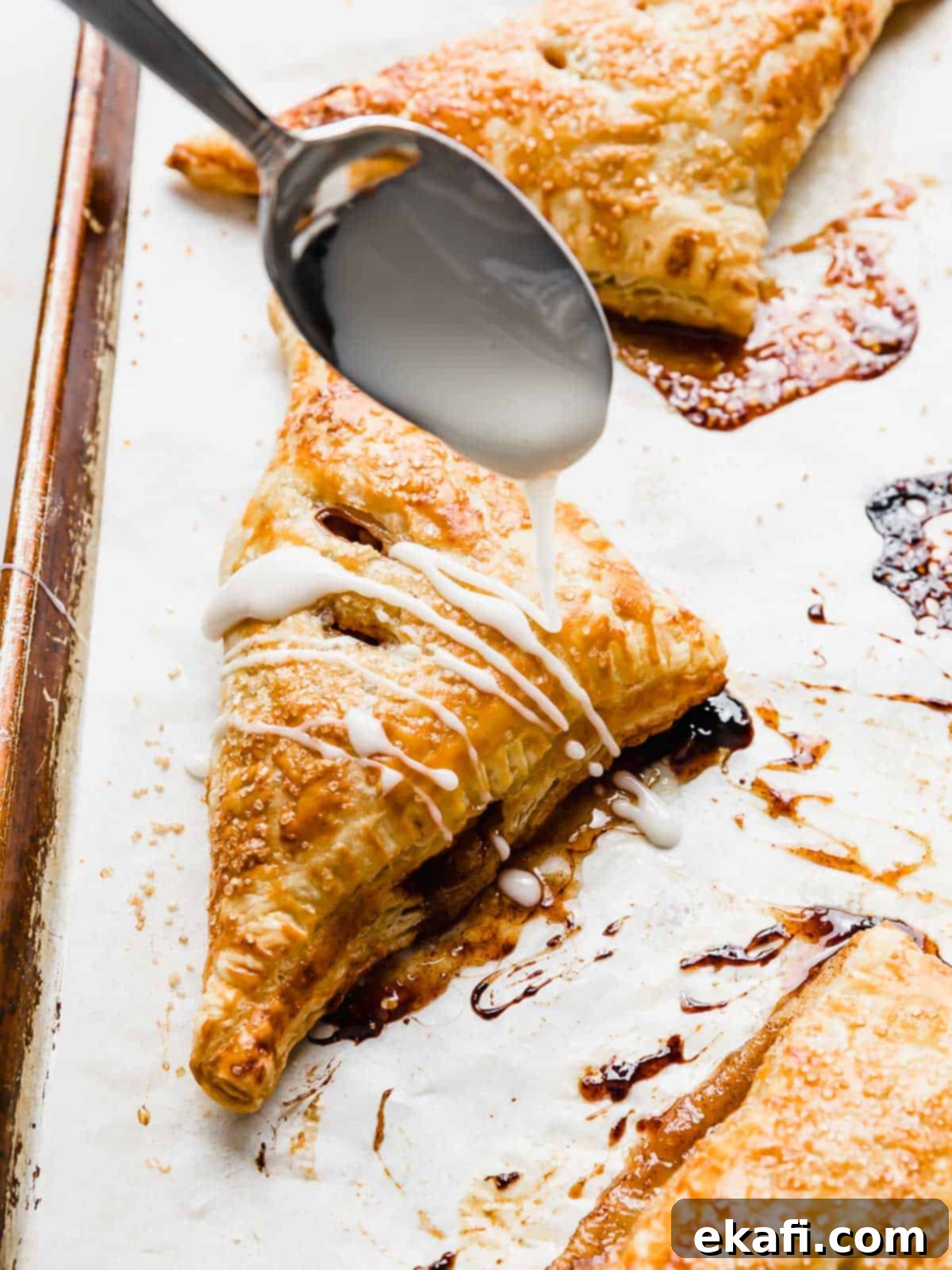 Flaky Apple Turnovers 13 A spoon drizzling glaze overtop a Puff Pastry Apple Turnover.