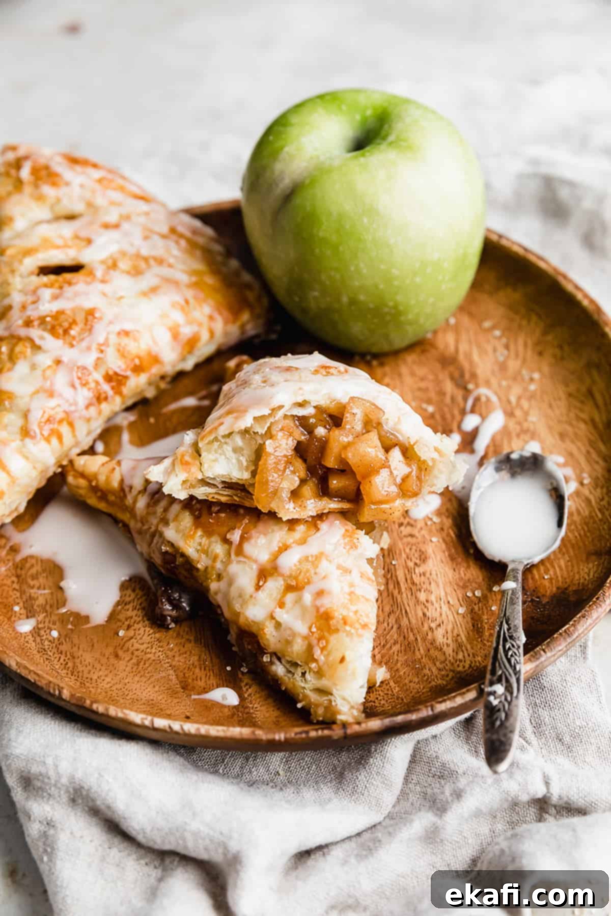 Flaky Apple Turnovers 14 A Puff Pastry Apple Turnover cut in half, on a brown plate, topped with a glaze.