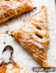 Flaky Apple Turnovers 15 A glazed Puff Pastry Apple Turnover on a white parchment paper.