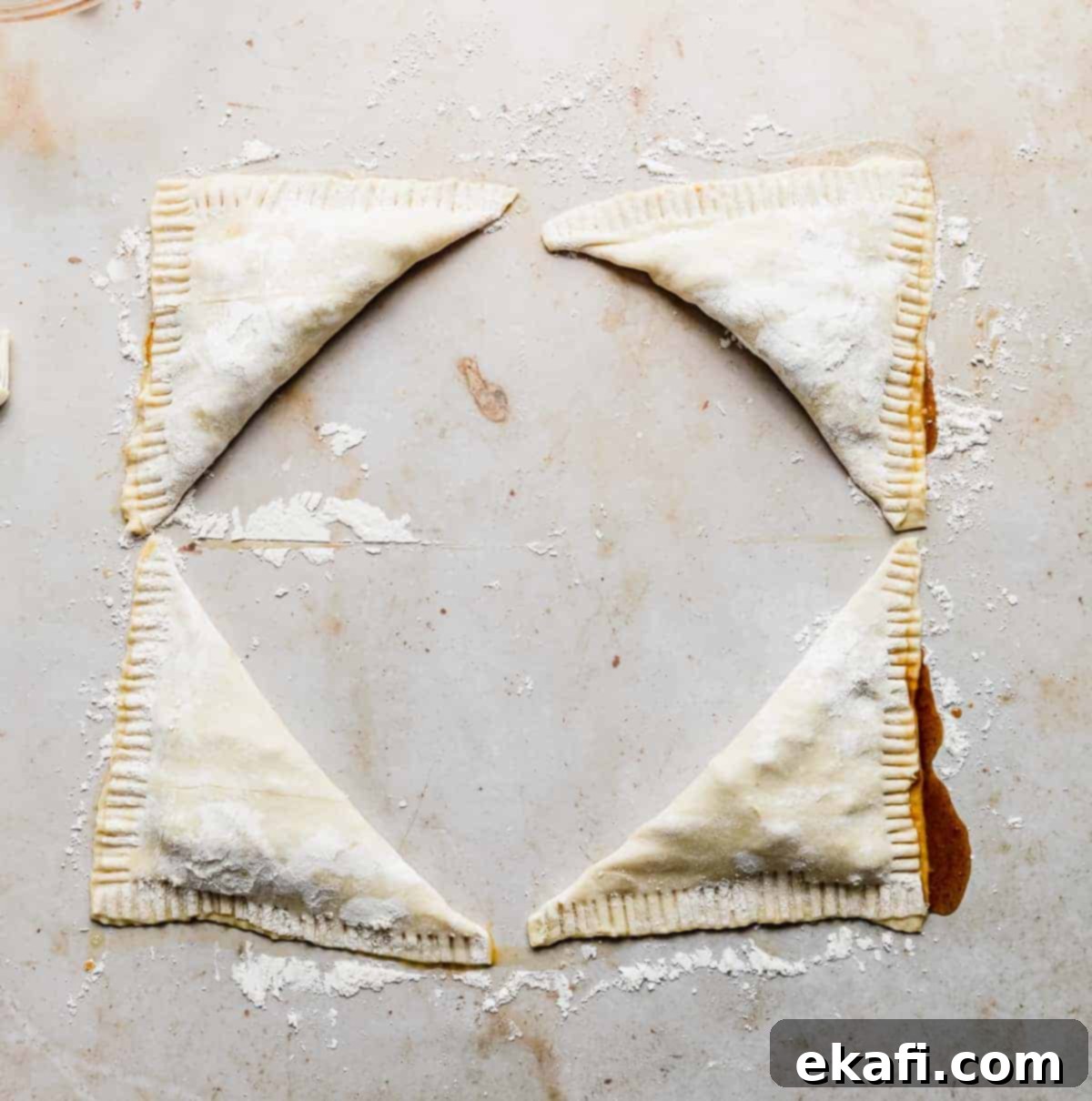 Flaky Apple Turnovers 10 Four squares of unbaked triangular Puff Pastry Apple Turnovers on a cream marbled background.