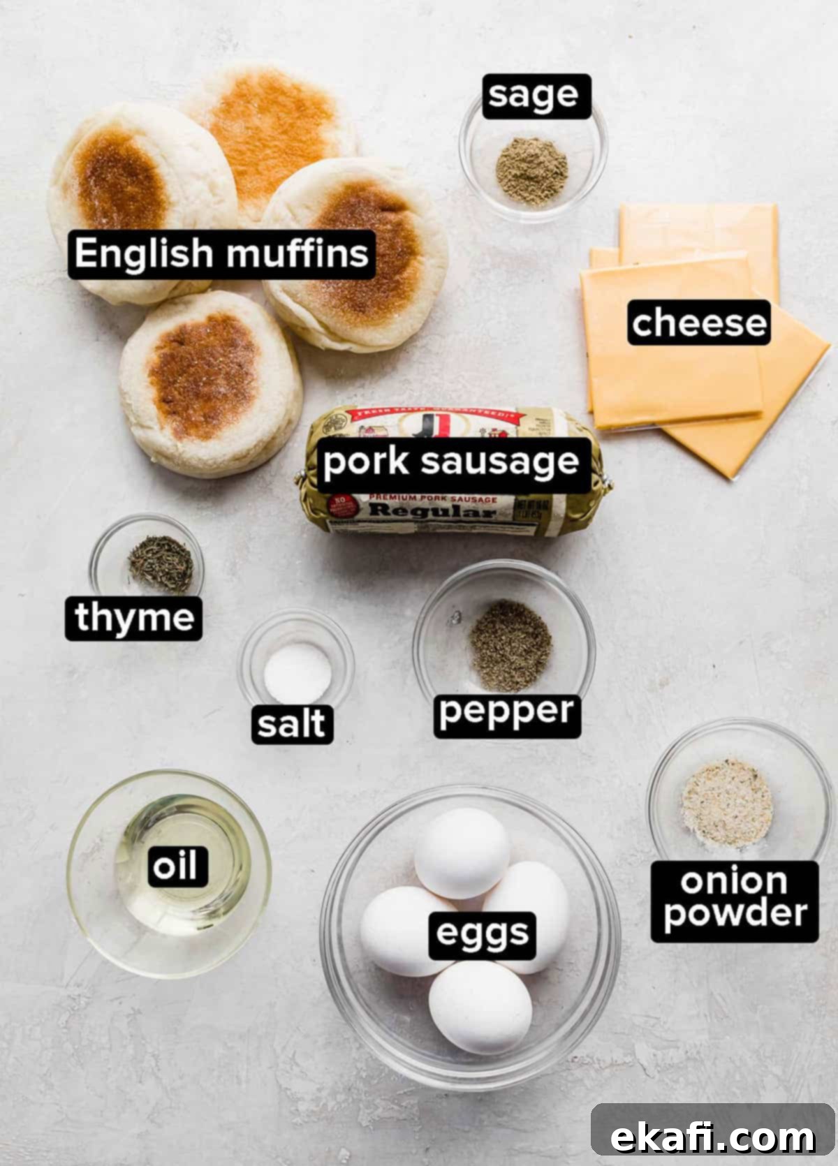 From Scratch Sausage and Egg Breakfast Sandwich 3 An overhead shot of all the fresh ingredients for homemade Sausage and Egg McMuffins laid out on a gray background, including ground pork, English muffins, eggs, American cheese, and a selection of dried herbs and spices.