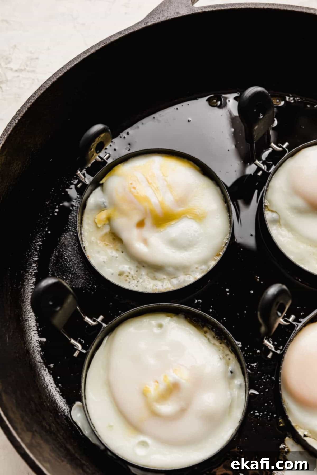 From Scratch Sausage and Egg Breakfast Sandwich 9 A single egg perfectly cooking within an egg ring in a black non-stick skillet, with steam rising from the pan.