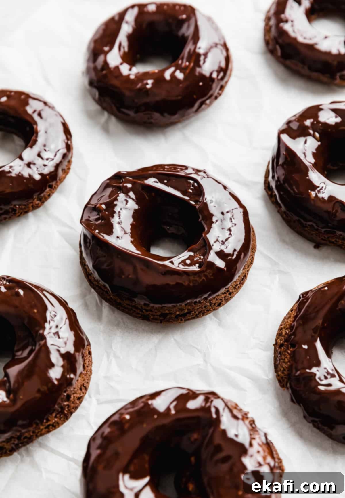 Ultimate Chocolate Donuts 12 A freshly glazed chocolate doughnut, glistening with rich chocolate ganache, presented on a white background, inviting a delicious bite.