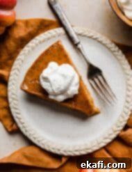 Pure Pumpkin Custard 11 Overhead photo of a slice of whipped cream topped Crustless Pumpkin Pie on a plate with a fork to the side, ready for tasting.