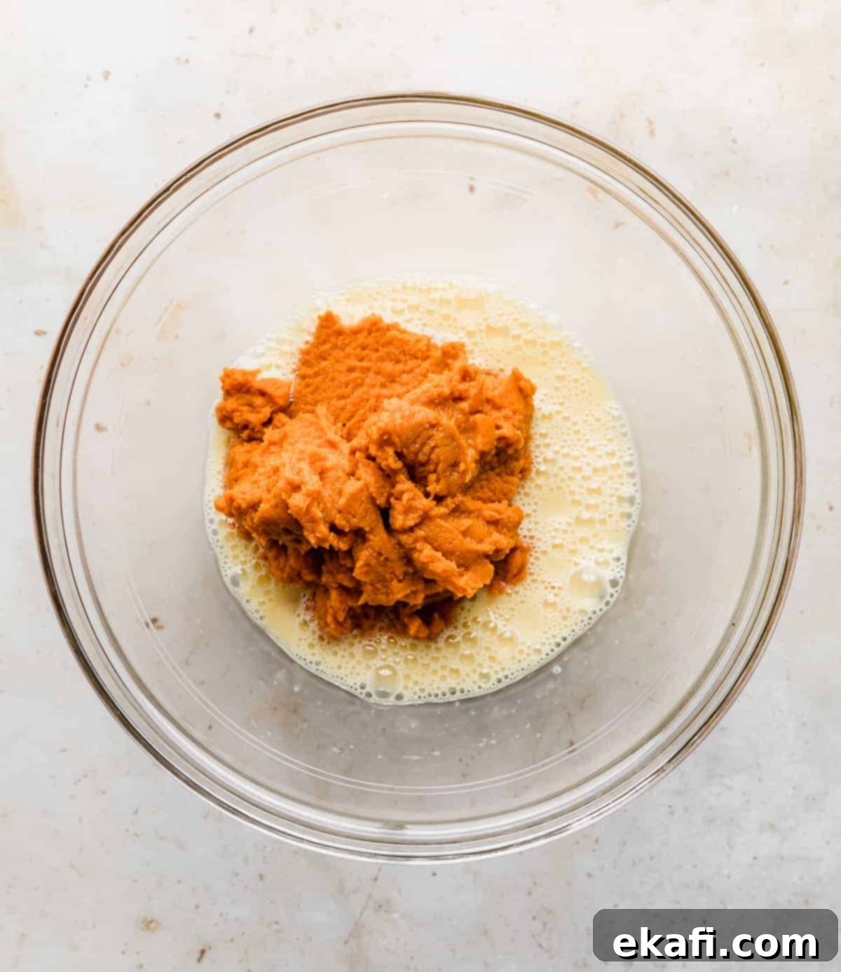 Pure Pumpkin Custard 4 A glass bowl showcasing canned pumpkin puree alongside freshly whipped eggs, ready to be combined for the pie filling.