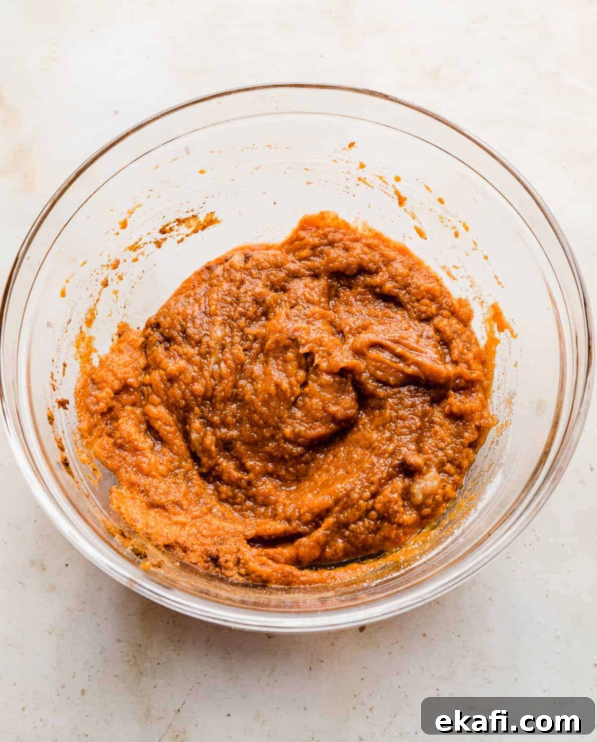 Pure Pumpkin Custard 6 A rich, thick orange mixture for making Crustless Pumpkin Pie in a clear glass bowl, showcasing its creamy texture before baking.