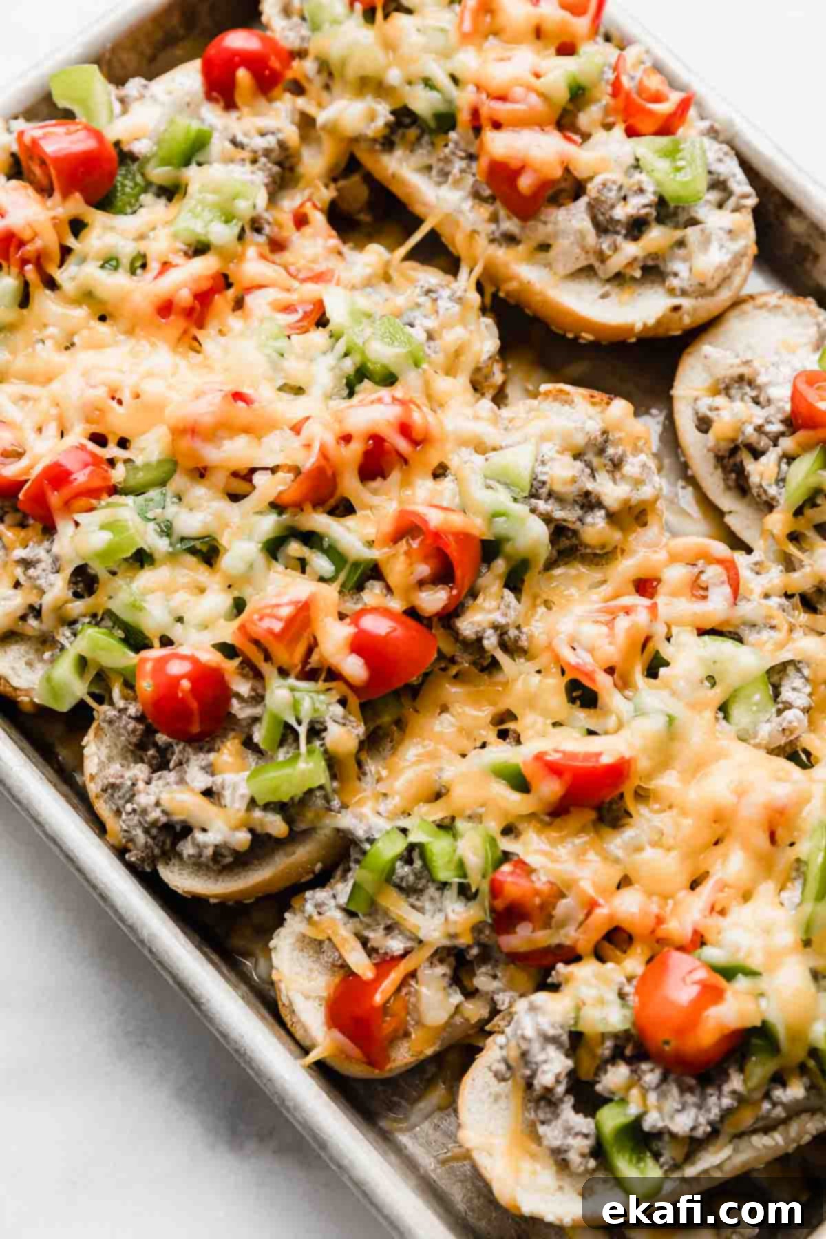 Beef Stroganoff Sandwich 2 Beef Stroganoff Sandwiches on a baking sheet, each hoagie bun topped with ground beef mixture, diced tomatoes and green peppers, and melted cheddar cheese.
