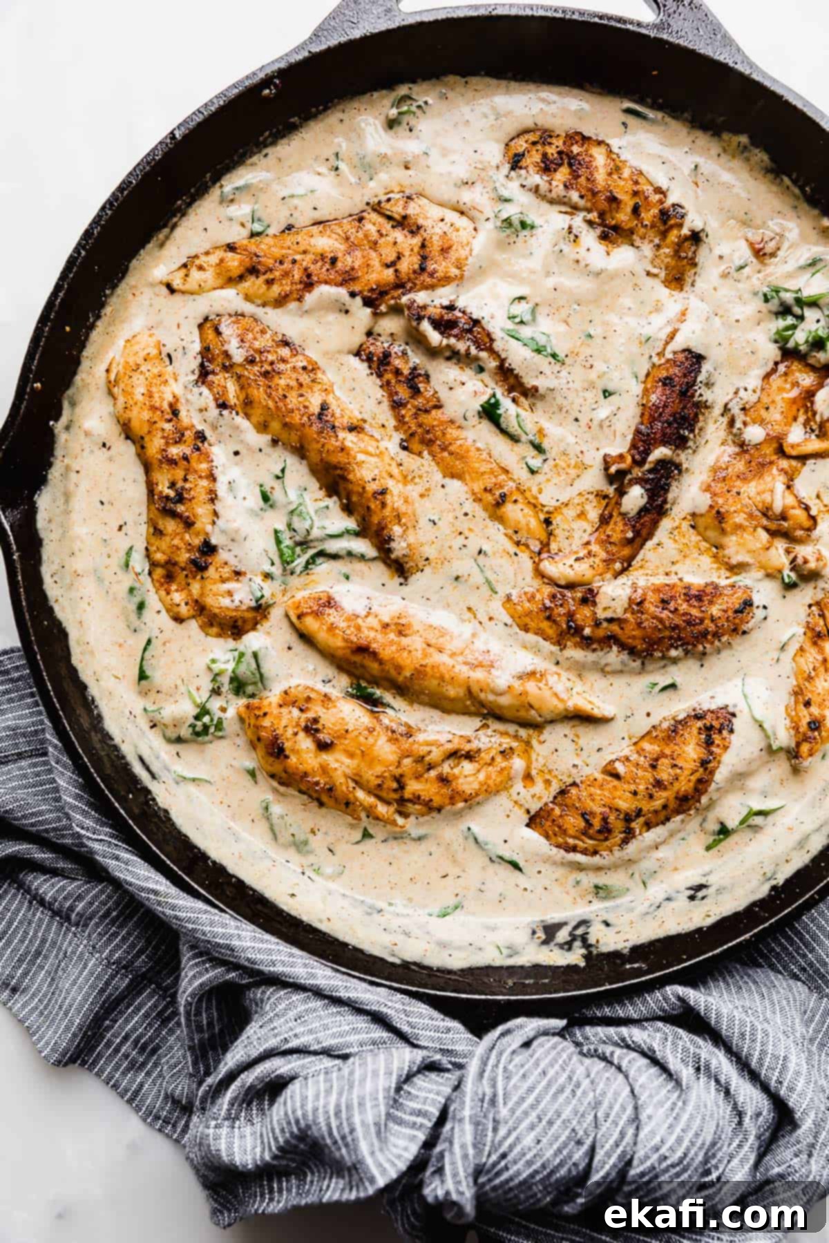 Tuscan Garlic Cream Chicken 2 A black cast iron skillet full of a Creamy Tuscan Chicken Recipe swimming in a tan colored gravy.