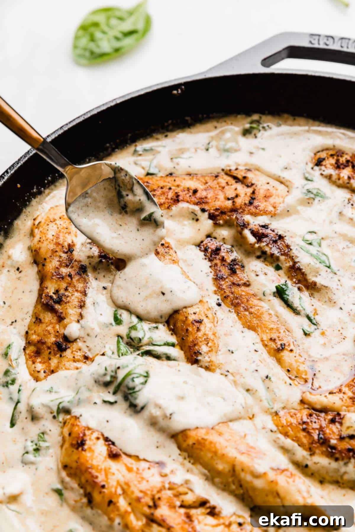 Tuscan Garlic Cream Chicken 8 A spoon pouring a tuscan chicken gravy overtop chicken tender pieces in a skillet.