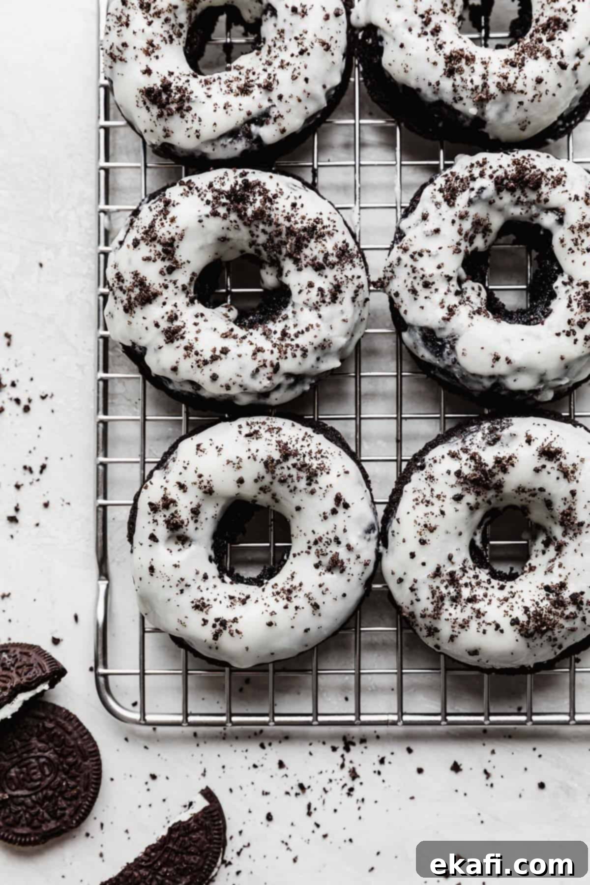 Cookies and Cream Donuts 12 White frosting topped Oreo Donuts with Oreo crumbs overtop, on a wire rack.