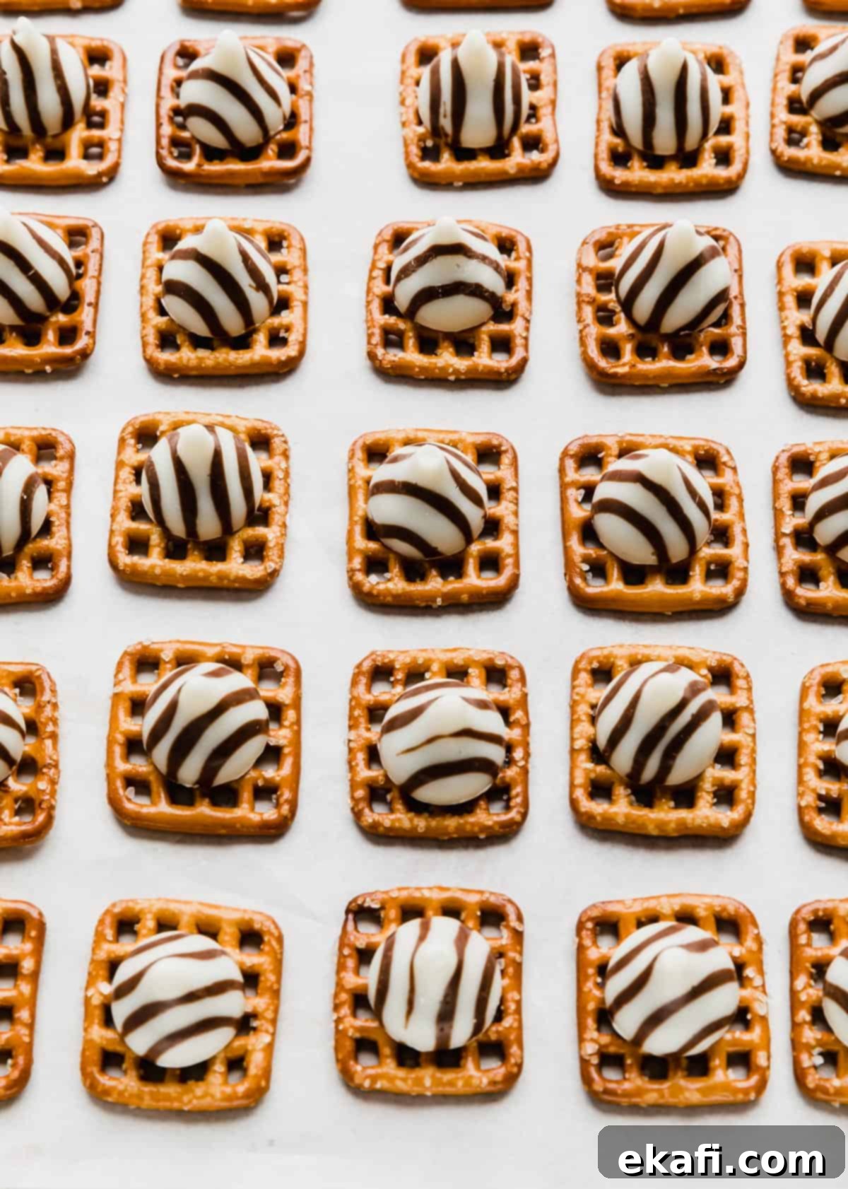 Christmas Pretzel Hugs 4 Square pretzels topped with unwrapped Hershey's Hug candies on a baking sheet.