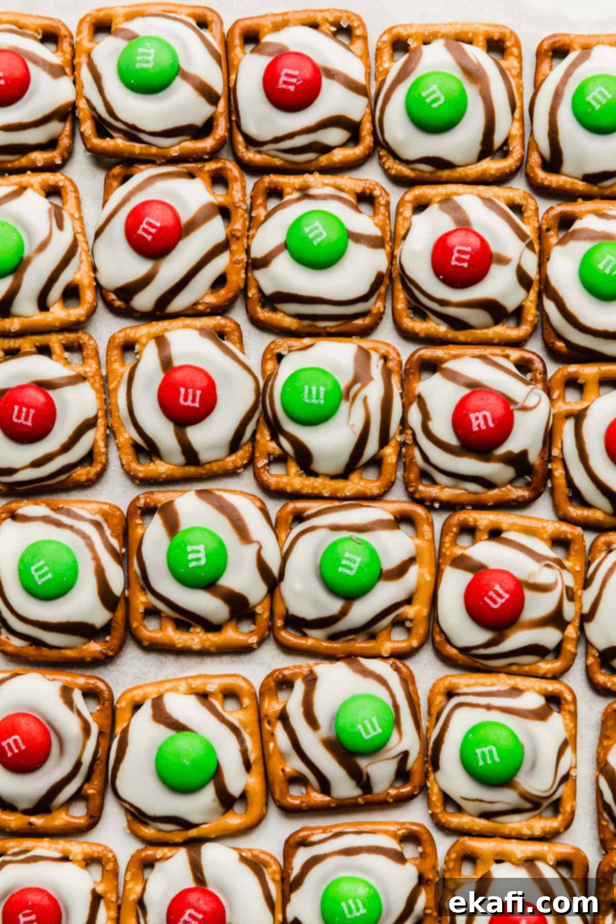 Christmas Pretzel Hugs 5 Red and green colored M&M's on top of melted hug candies on a square pretzel, cooling on a baking sheet.