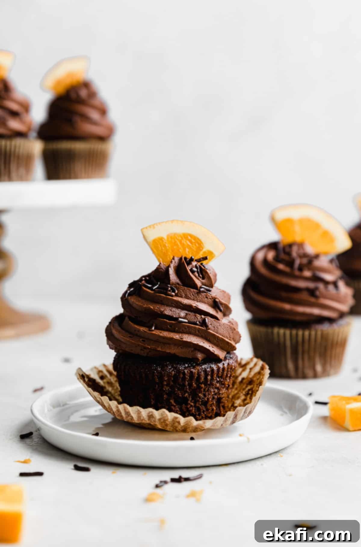 Zesty Chocolate Orange Delights 11 Chocolate frosting topped Chocolate Orange Cupcakes with a fresh orange slice stuck into the frosting, on a white background.