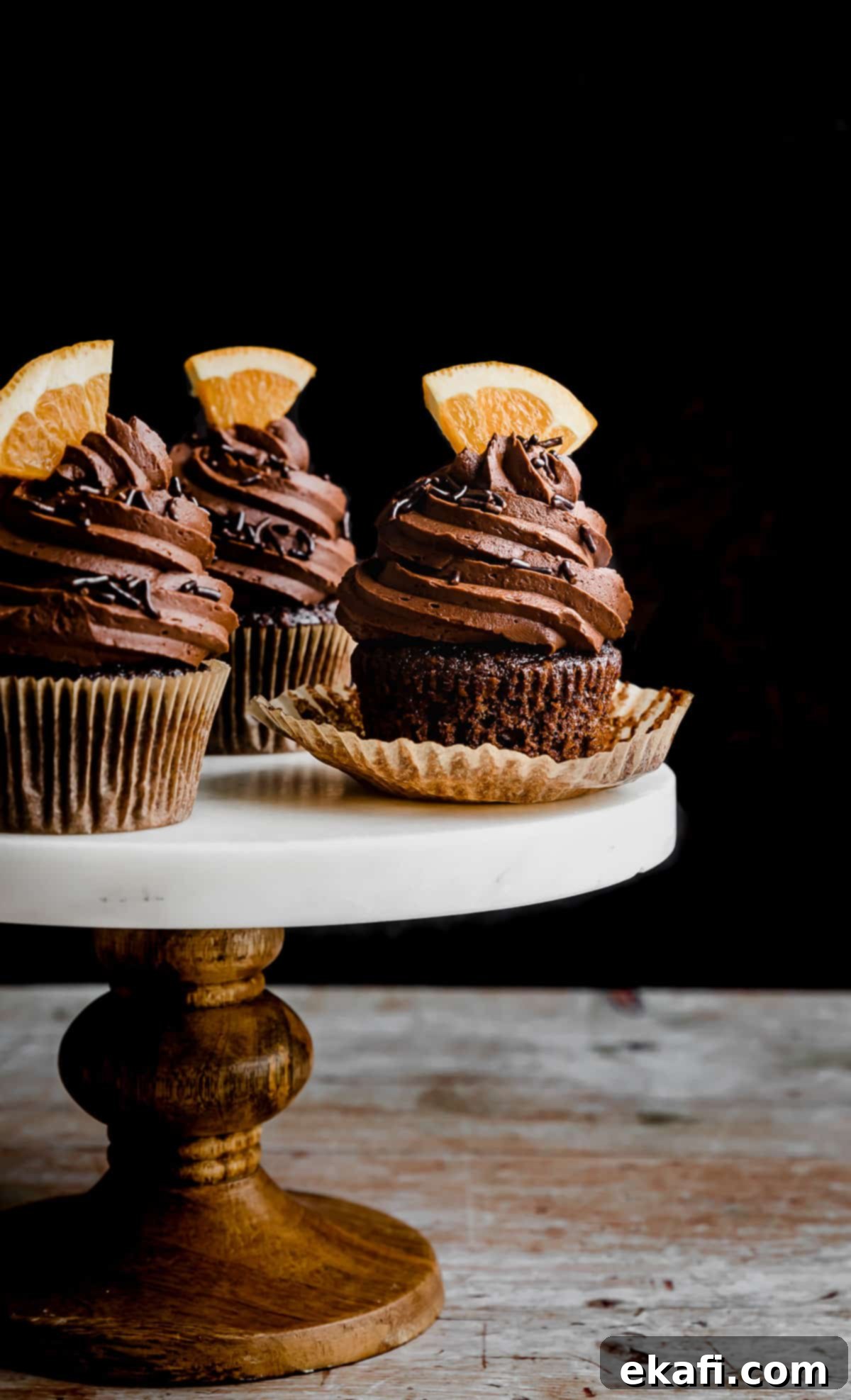 Zesty Chocolate Orange Delights 12 Chocolate Orange Cupcakes on a white marble topped cake stand against a black background.