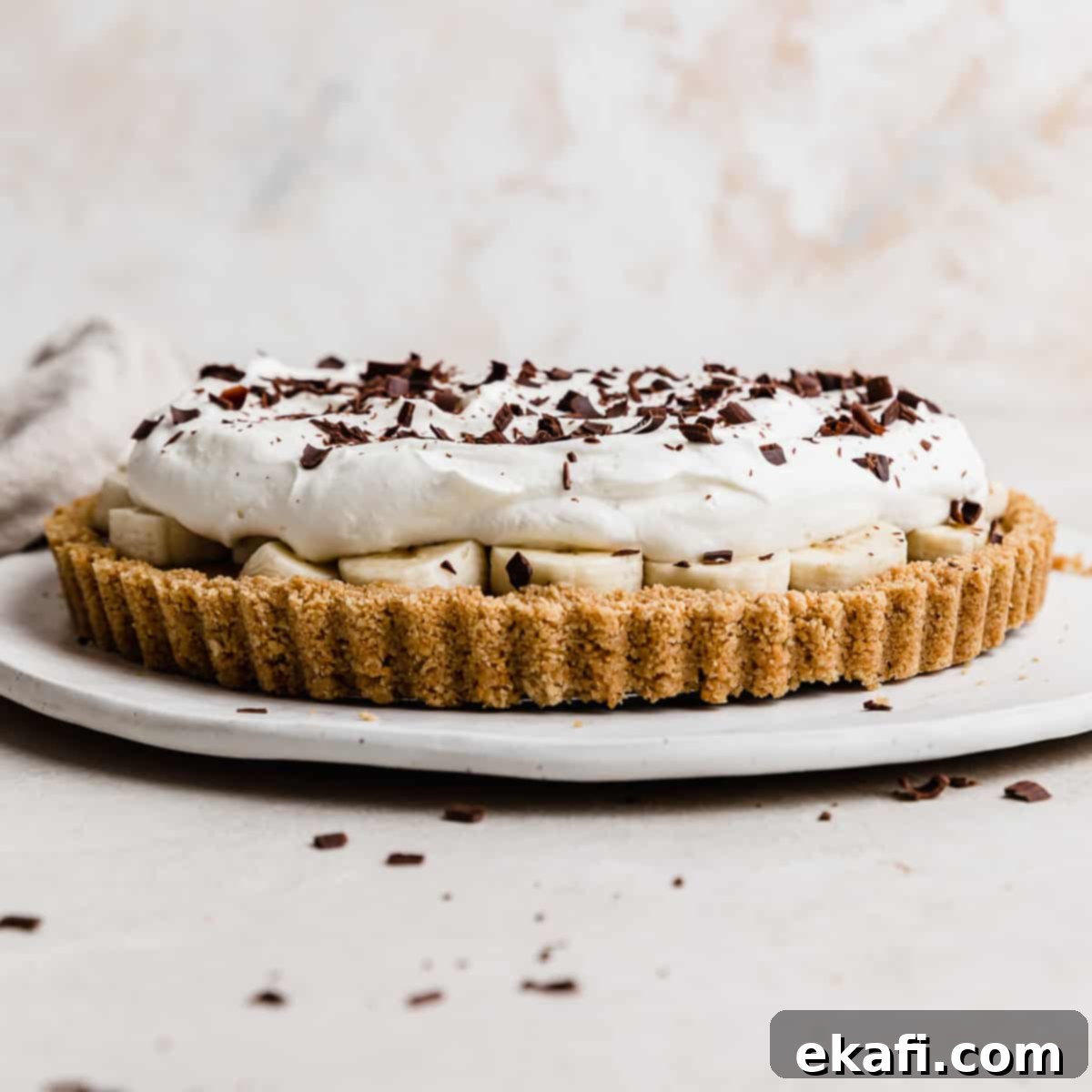 Οι Απόλυτες Πίτες Ευχαριστιών 12 Μια Banoffee Pie σε λευκό πιάτο, με σαντιγί και ξύσματα σοκολάτας από πάνω.