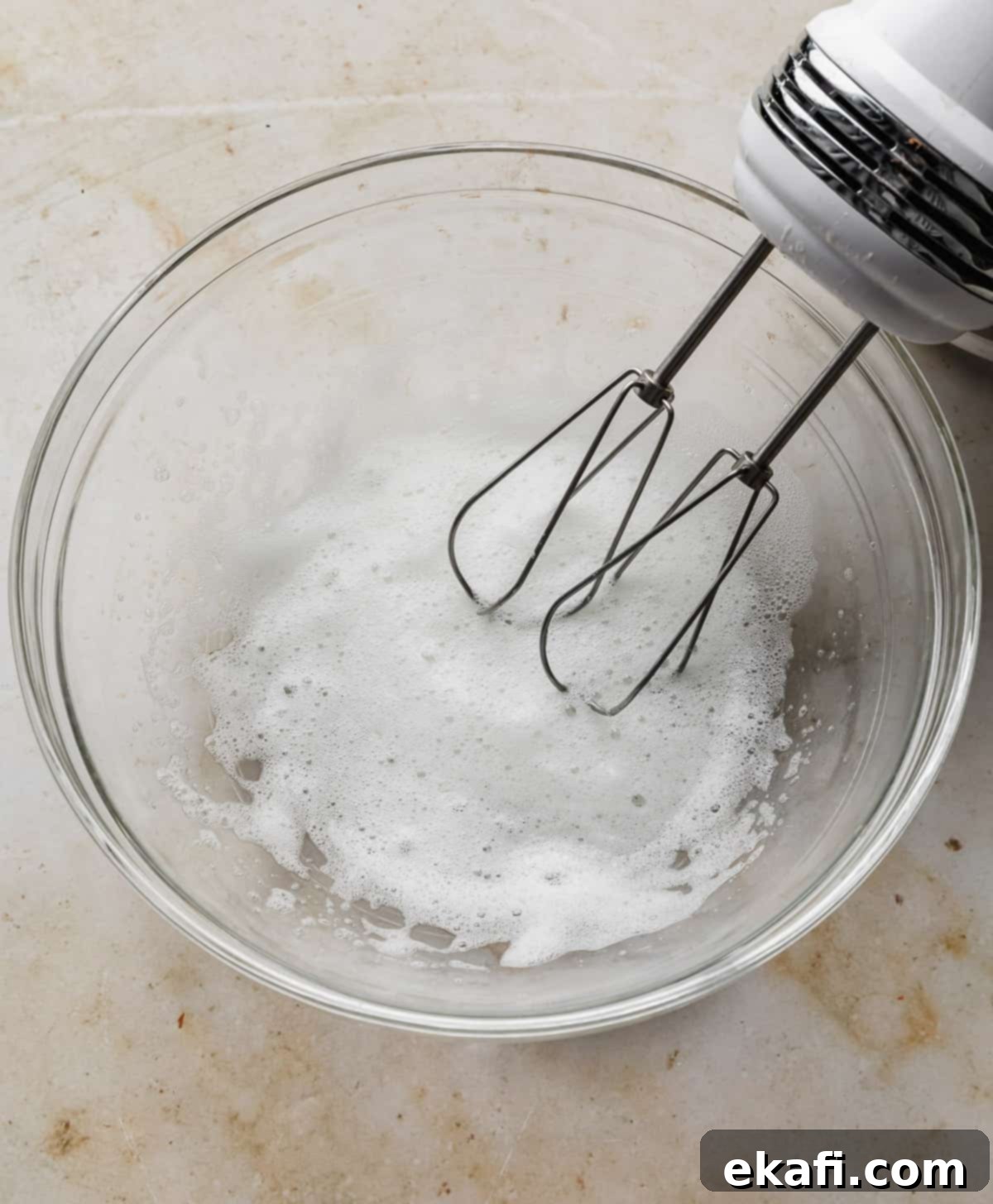 Sweet Glazed Pecans 5 A hand mixer whipping egg whites and water until frothy in a clear glass bowl.