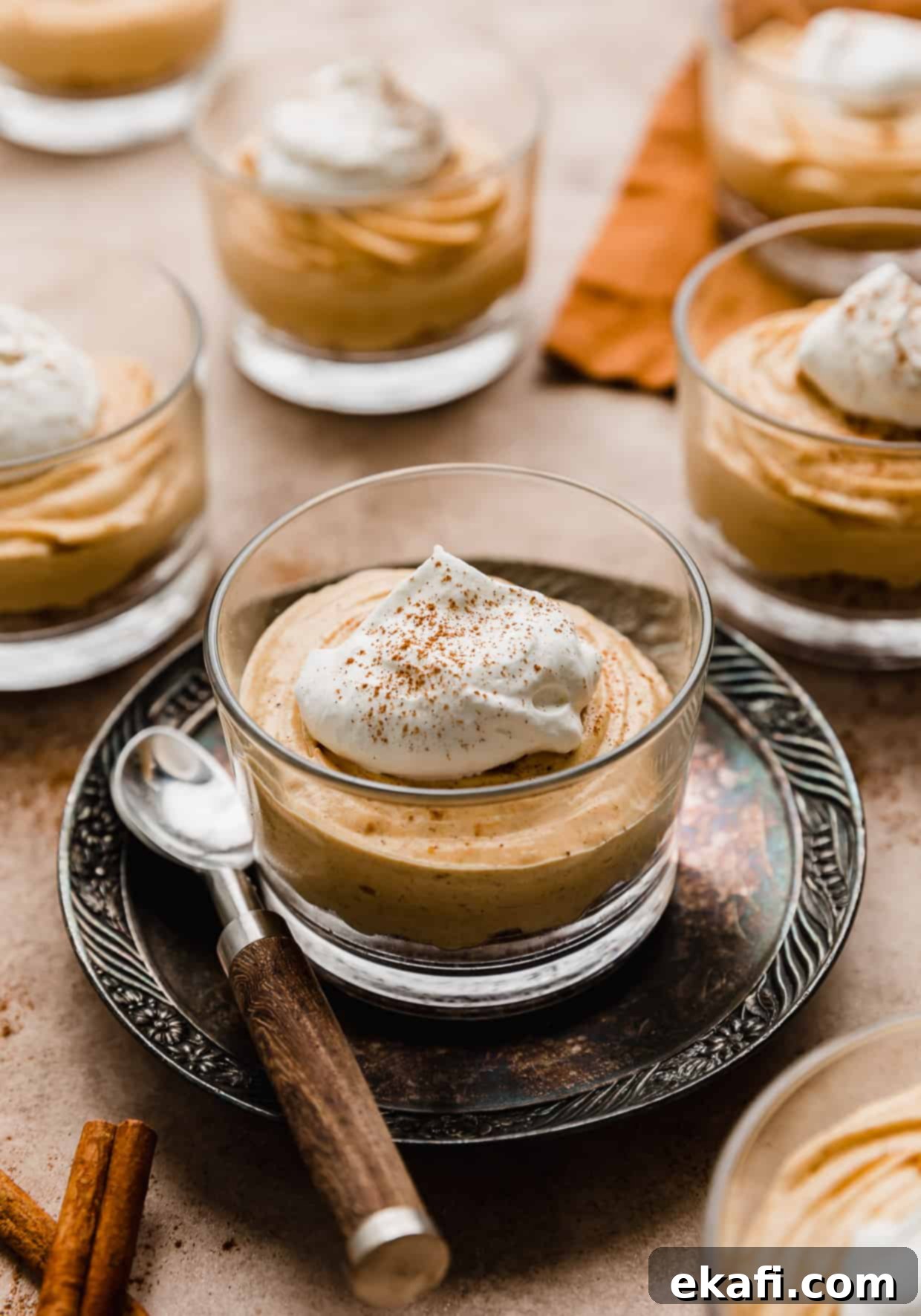 Quick Pumpkin Cheesecake Minis 7 A small glass cup filled halfway with a no-bake pumpkin cheesecake filling and topped with a dollop of whipped cream.