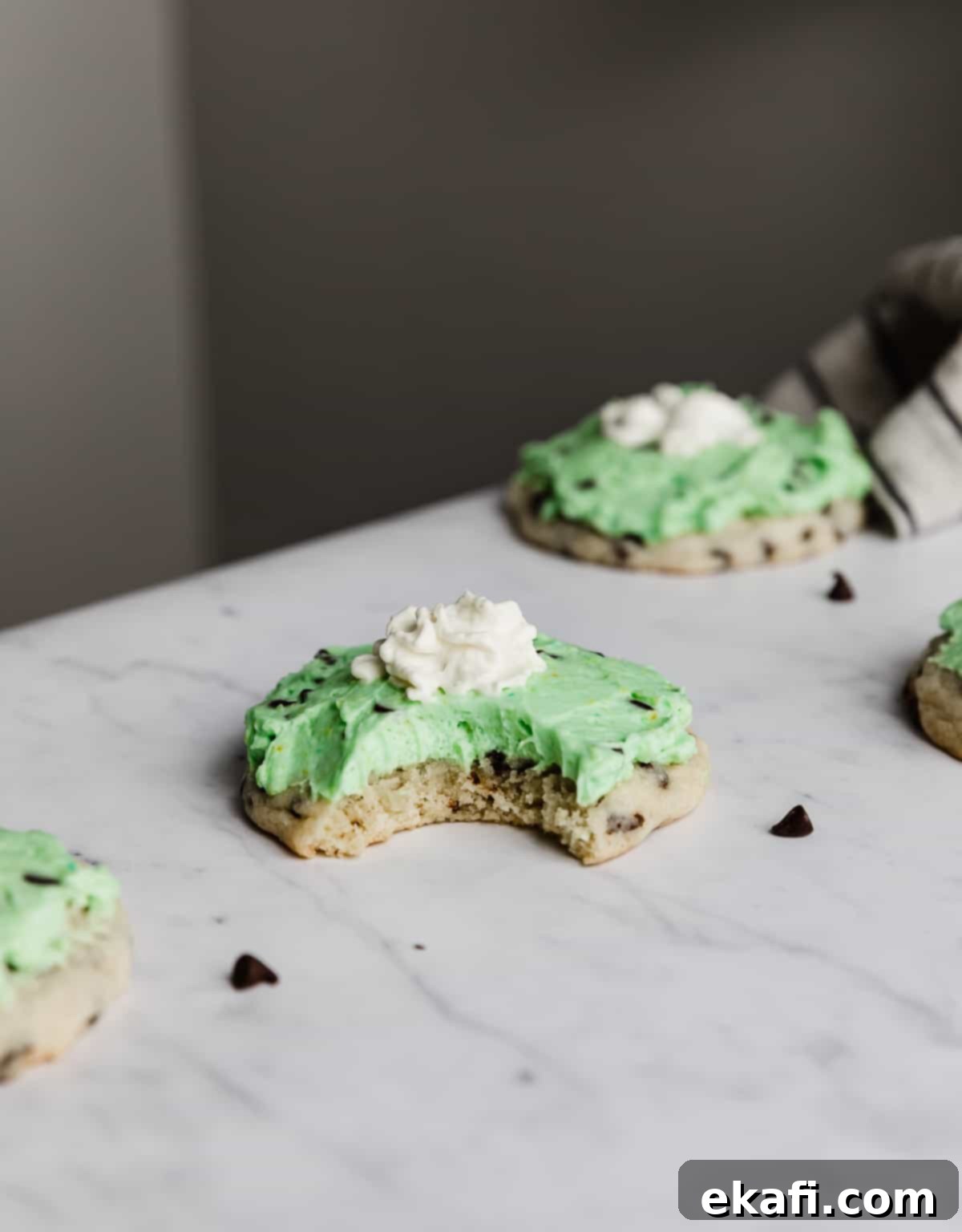 Crumbl's Mint Chip Ice Cream Cookie Delight 2 A Crumbl Mint Chip Ice Cream Cookie topped with a green frosting and dollop of whip cream on a white marble table.
