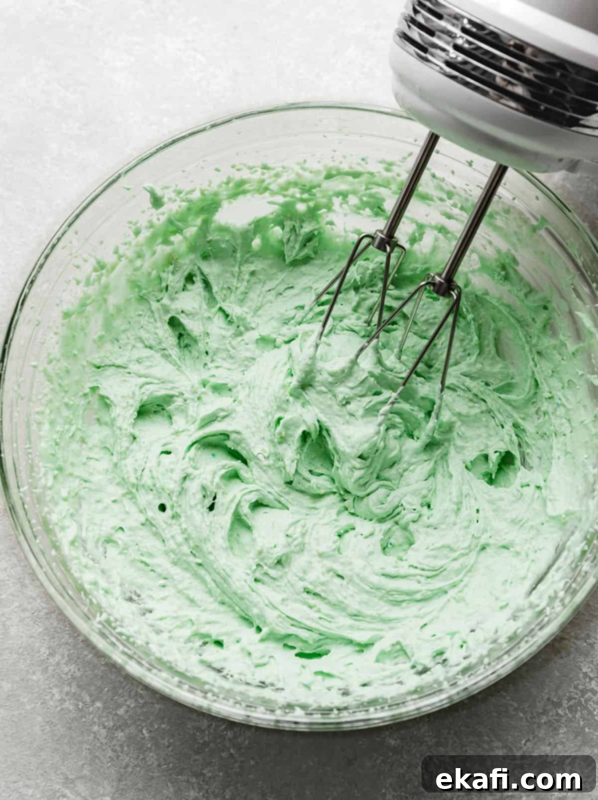 Crumbl's Mint Chip Ice Cream Cookie Delight 11 A hand mixer beating together a mint colored mousse to frost Crumbl Mint Chip Ice Cream Cookies.