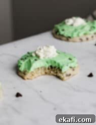 Crumbl's Mint Chip Ice Cream Cookie Delight 16 A bite taken out of a copycat Crumbl Mint Chip Ice Cream Cookie that's topped with mint green frosting and a dollop of whip cream.