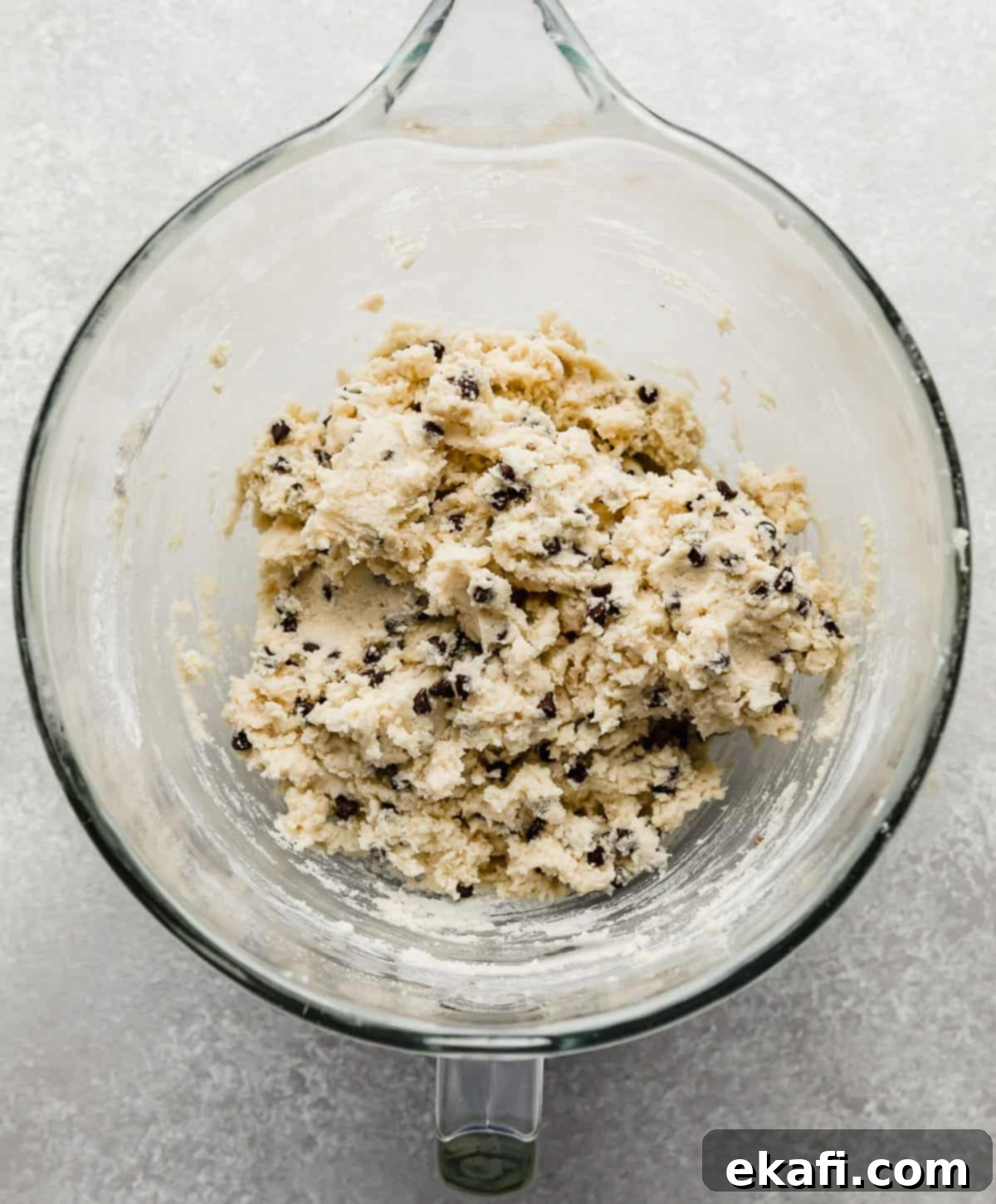 Crumbl's Mint Chip Ice Cream Cookie Delight 5 A glass mixing bowl with mini chocolate chips stirred into a sugar cookie dough.