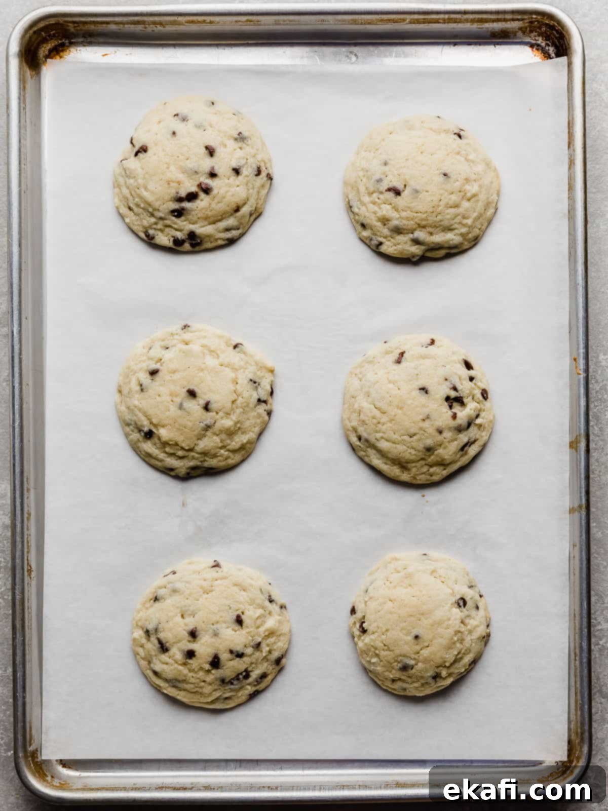 Crumbl's Mint Chip Ice Cream Cookie Delight 8 Six Mini chocolate chip studded sugar cookies on a white parchment lined baking sheet.
