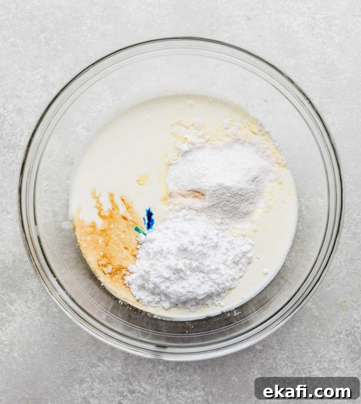 Crumbl's Mint Chip Ice Cream Cookie Delight 10 A glass bowl with heavy cream, powdered sugar, vanilla pudding powder, and blue food color drops in it.