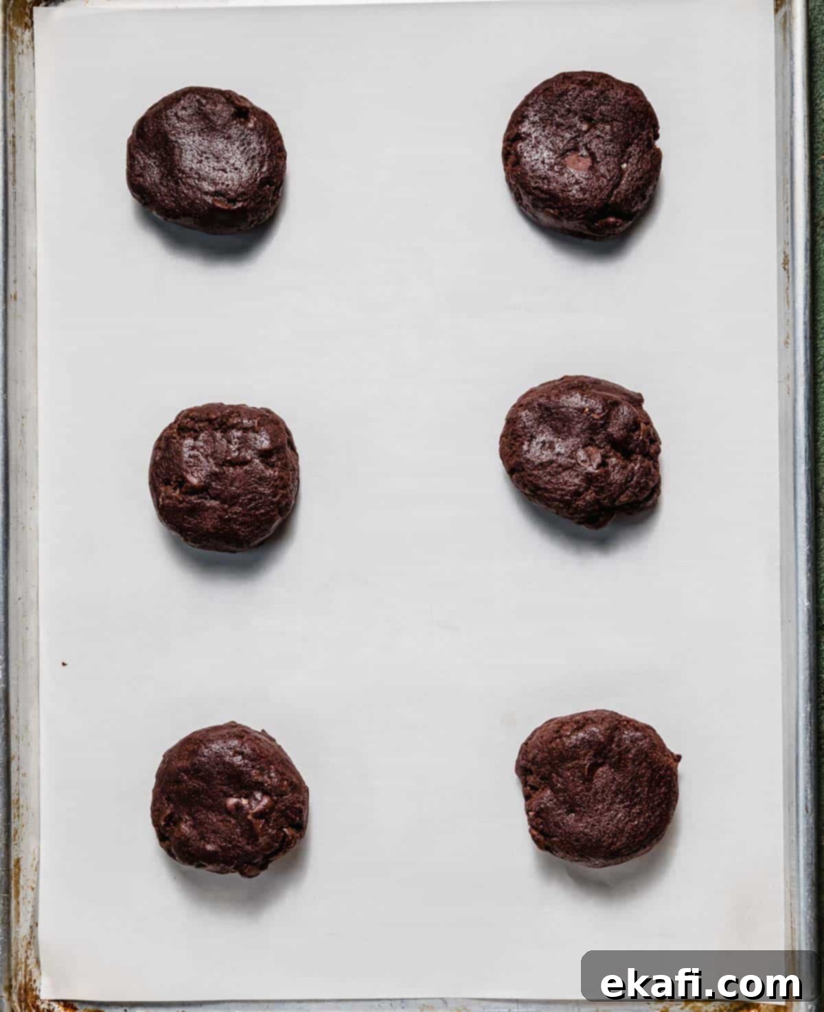 Chocolate Peppermint Bark Cookies 5 Six chocolate cookie dough balls on a white parchment lined baking sheet.