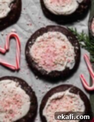Chocolate Peppermint Bark Cookies 10 Peppermint Bark Cookies topped with white chocolate and crushed candy canes, on a white parchment paper that's on a forest green background.