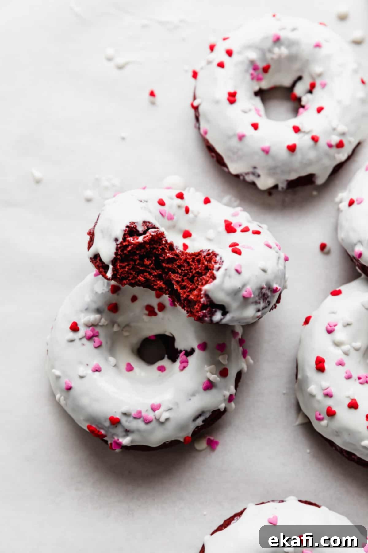 Κόκκινο Βελούδο Ντόνατς 2 Ντόνατς Red Velvet με επικάλυψη λευκής σοκολάτας και καρδιές τρούφας σε λευκό φόντο.