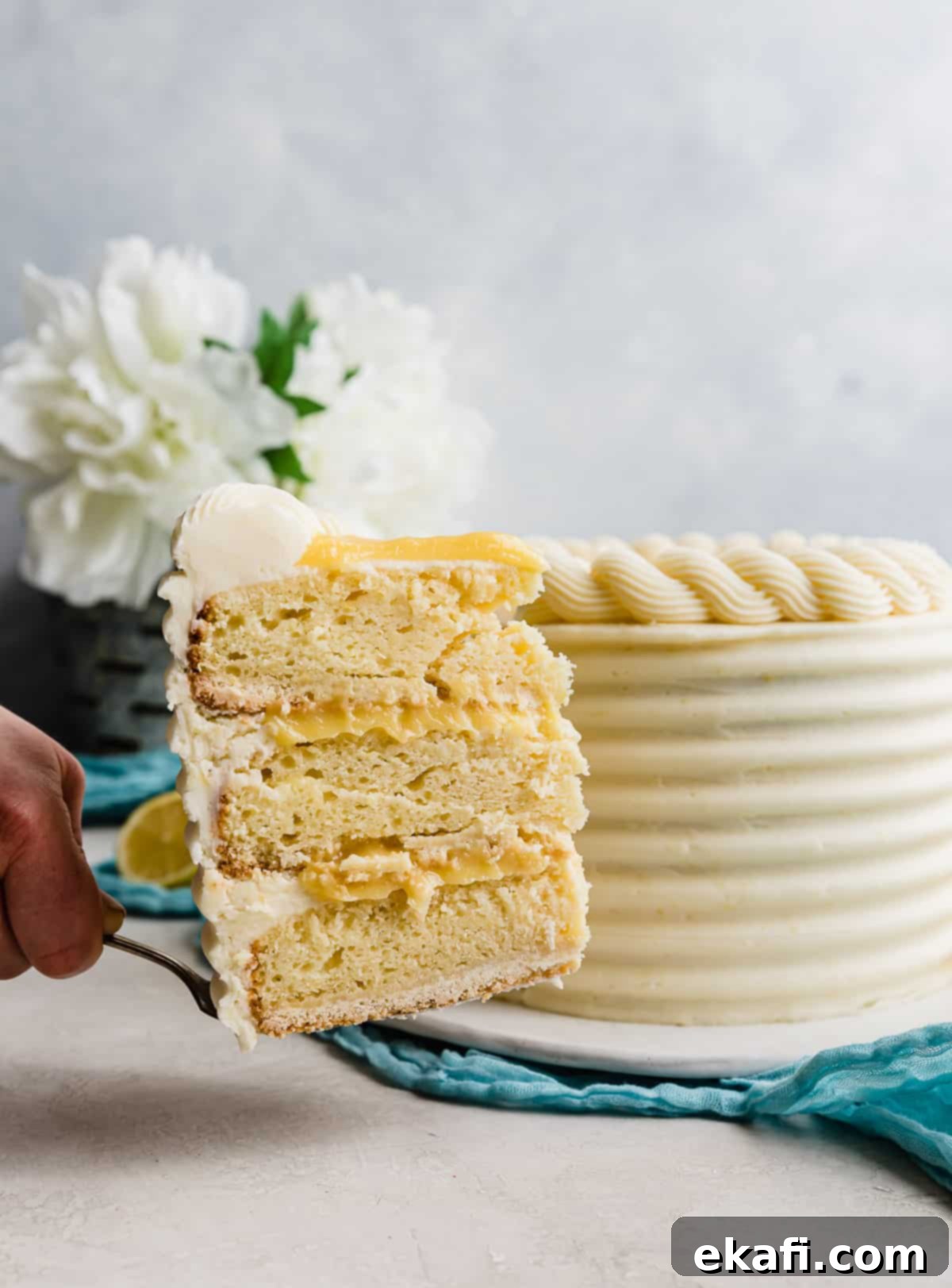 Zesty Lemon Bar Cake 2 A slice of lemon bar layer cake being held up in front of the full cake.