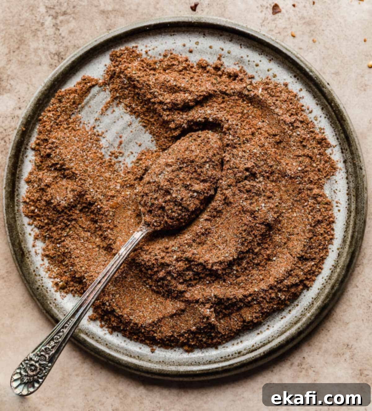 Mellow Fiesta Seasoning 5 Homemade Mild Taco Seasoning on a gray plate with a spoon scooping the powder, highlighting its fine texture.