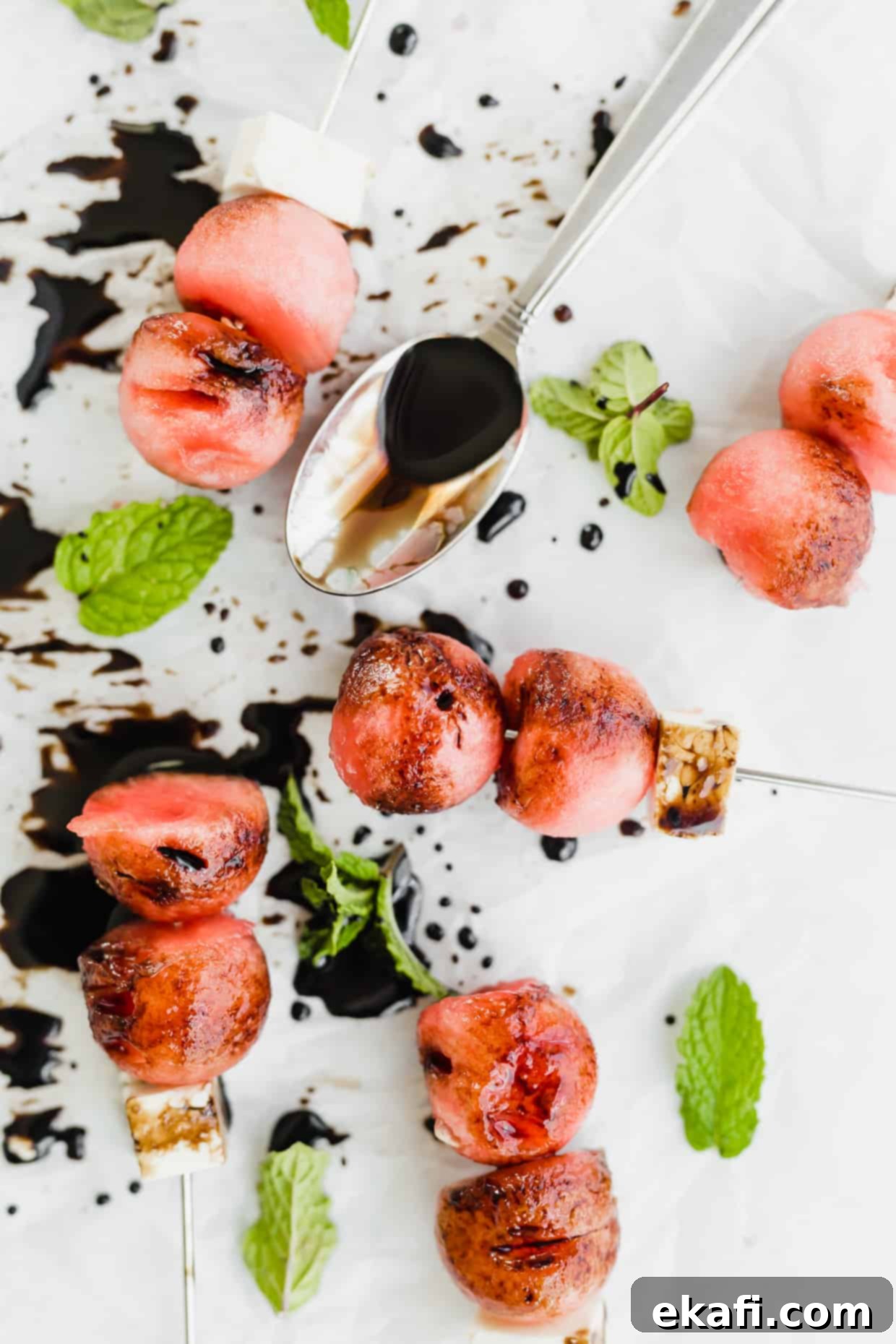 Cool Watermelon Sticks 9 Overhead photo of 2 watermelon balls and a block of feta on small skewers with glossy balsamic reduction drizzled overtop, garnished with fresh mint.