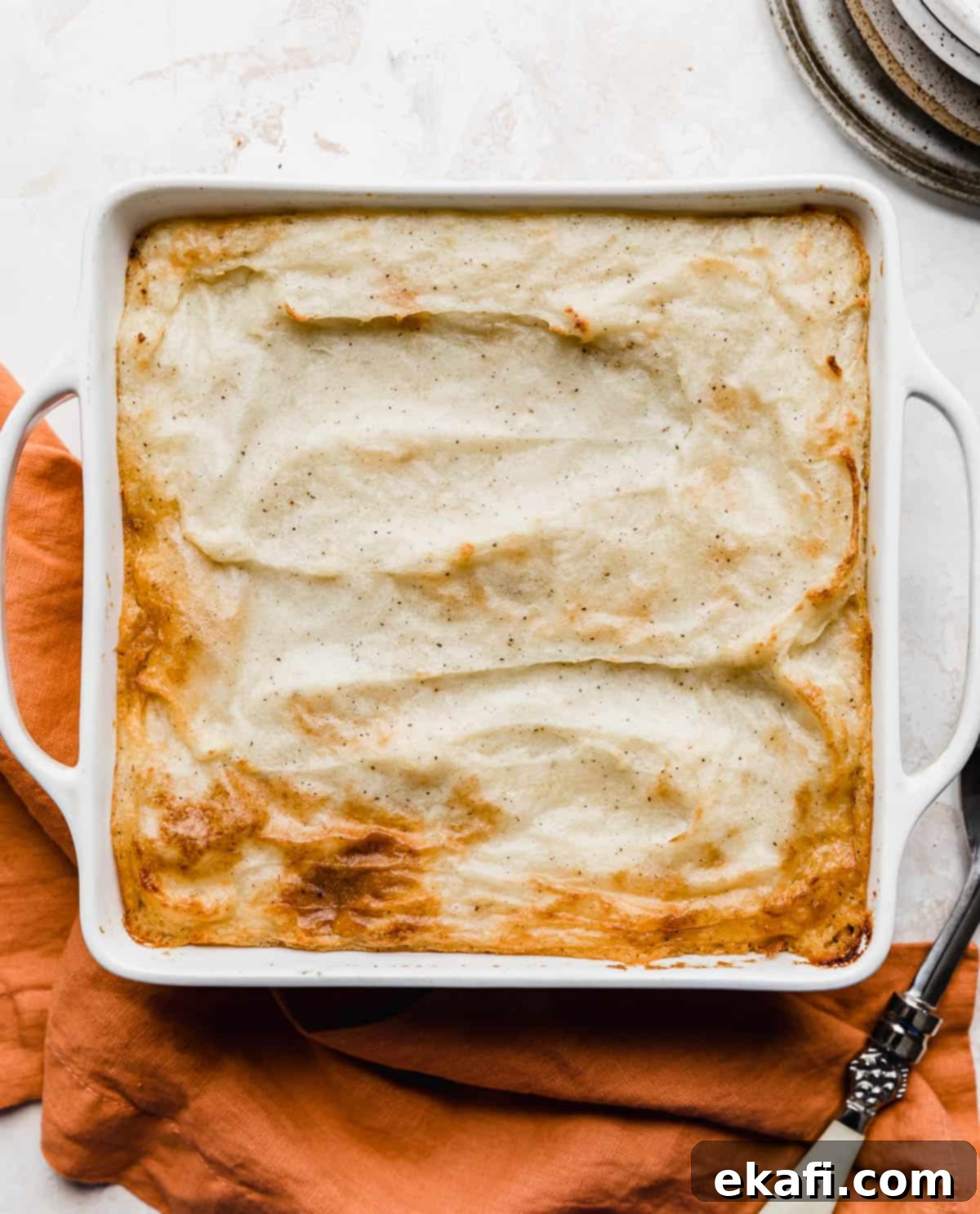 Hearty Lamb Potato Casserole 14 A perfectly baked Shepherd's pie recipe, showcasing its golden-brown mashed potato topping, presented on a rustic burnt orange napkin, ready to be served.