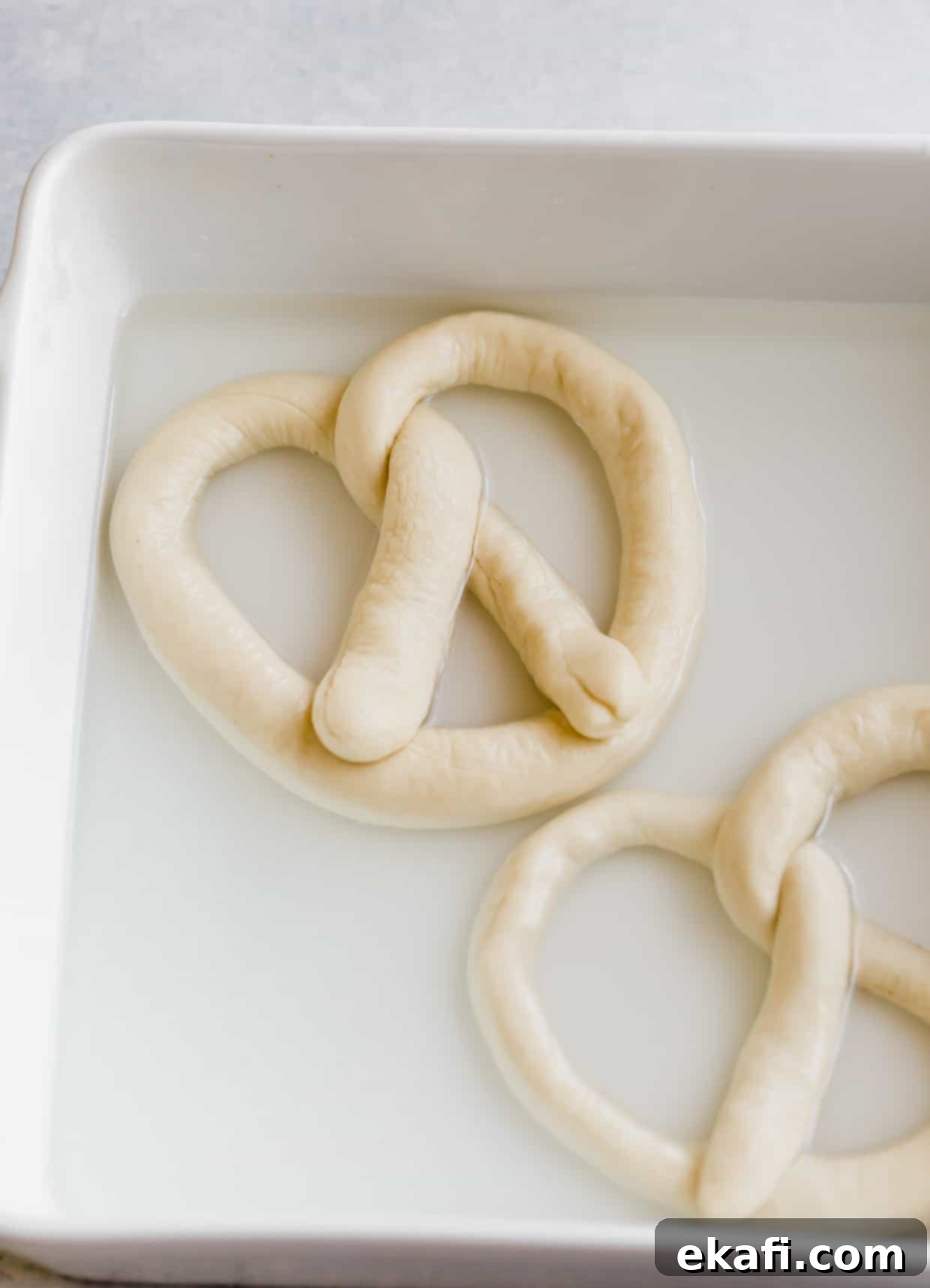 Perfect Homemade Soft Pretzels 7 An unbaked pretzel sitting in a baking soda and water bath, showing the importance of this step before baking.