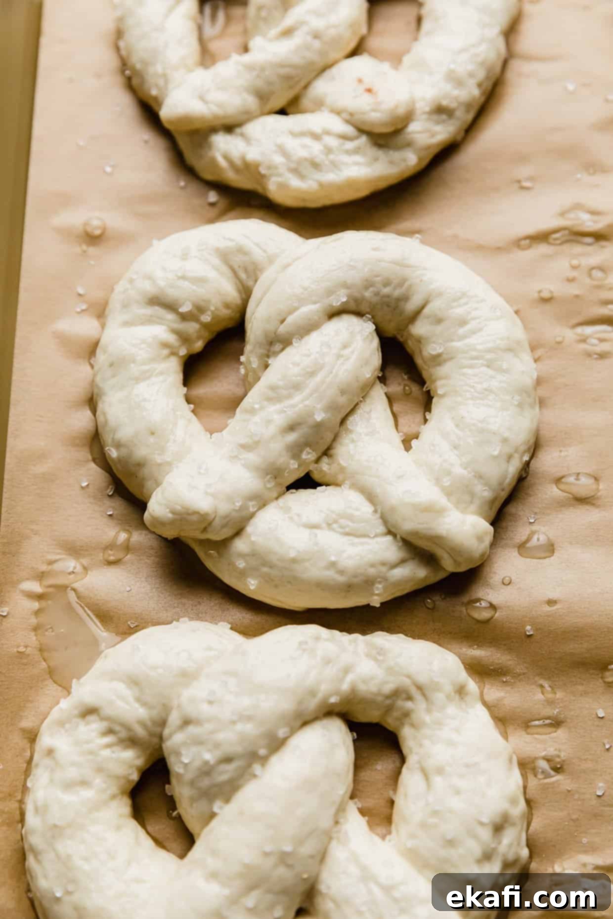 Perfect Homemade Soft Pretzels 8 A perfectly shaped unbaked pretzel, sprinkled with coarse salt, resting on a baking sheet lined with parchment paper, awaiting the oven.
